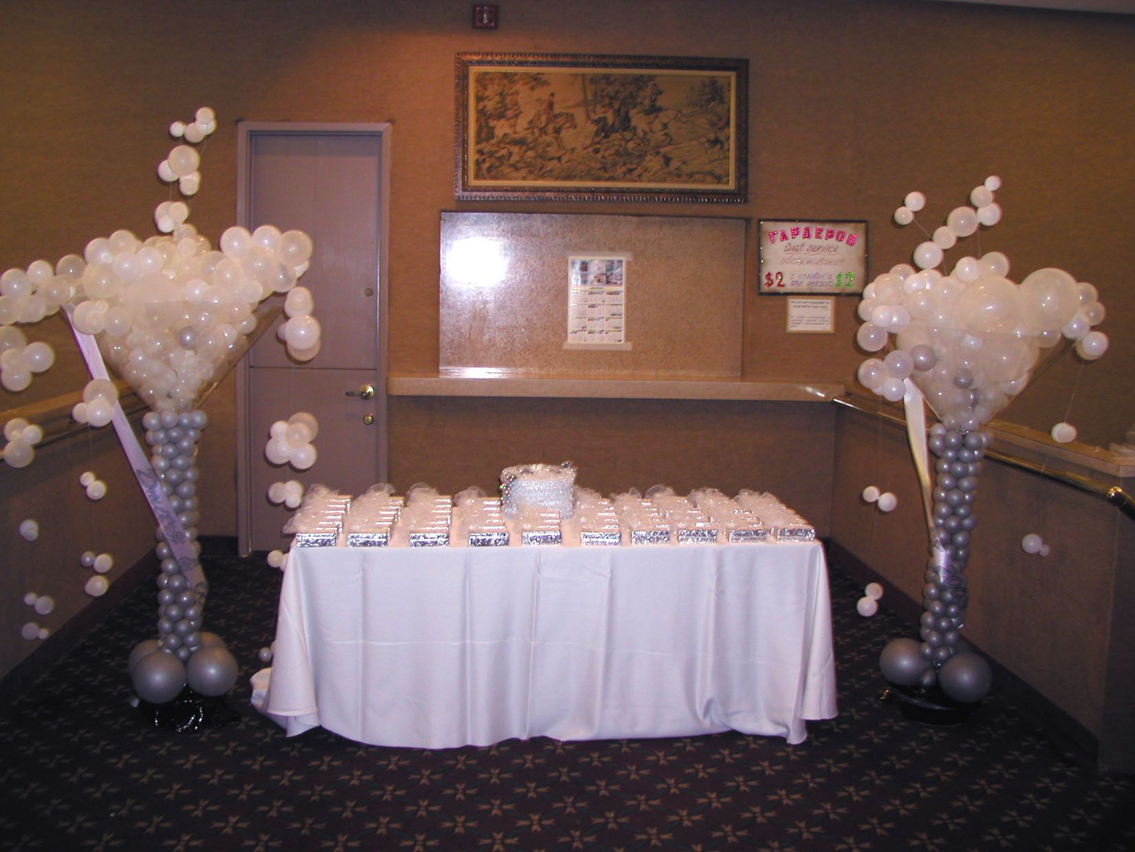 Reception area with a table covered in a white tablecloth and silver balloon columns flanking the sides.