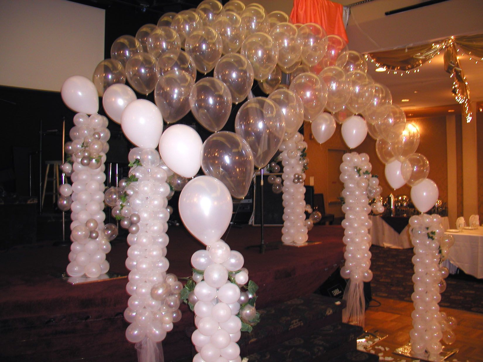 Balloon arch with clear and white balloons, decorated pillars in a party setting.