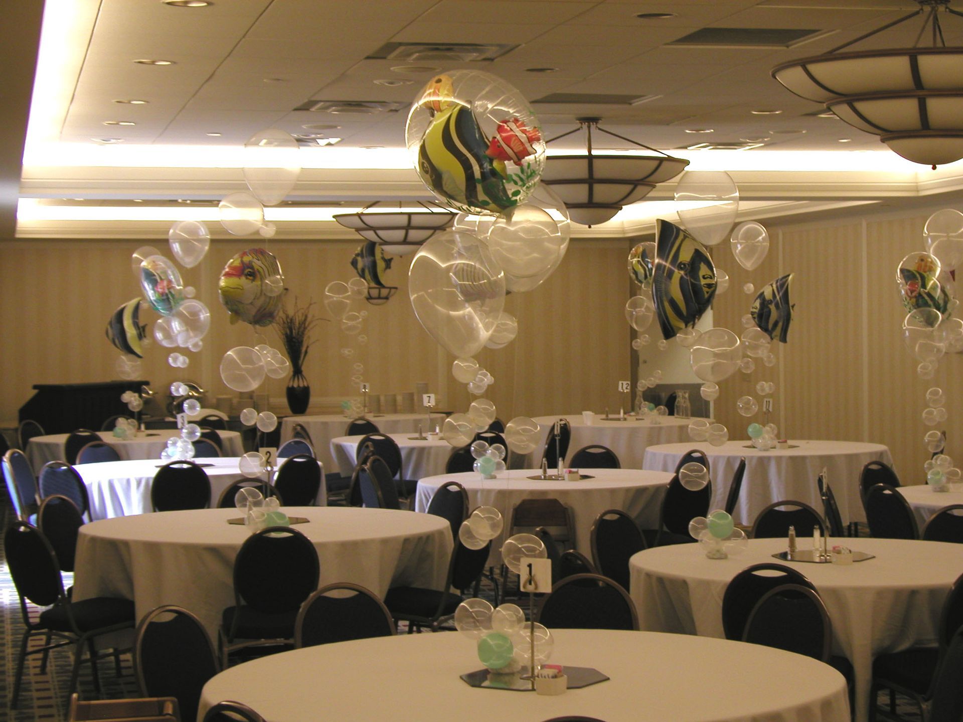 A ballroom decorated with fish-shaped balloons and clear bubbles; tables set with white tablecloths.