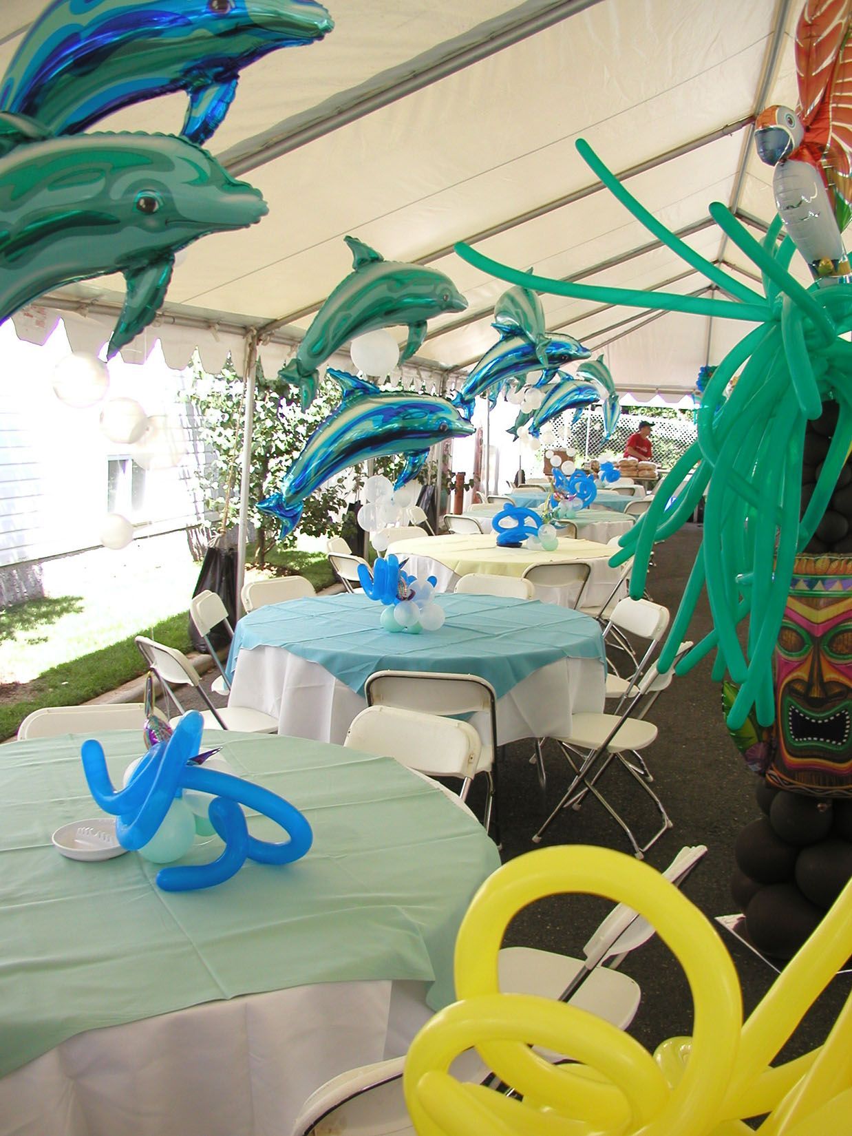 Party tent with dolphin balloons, tables with blue tablecloths, and balloon decorations.
