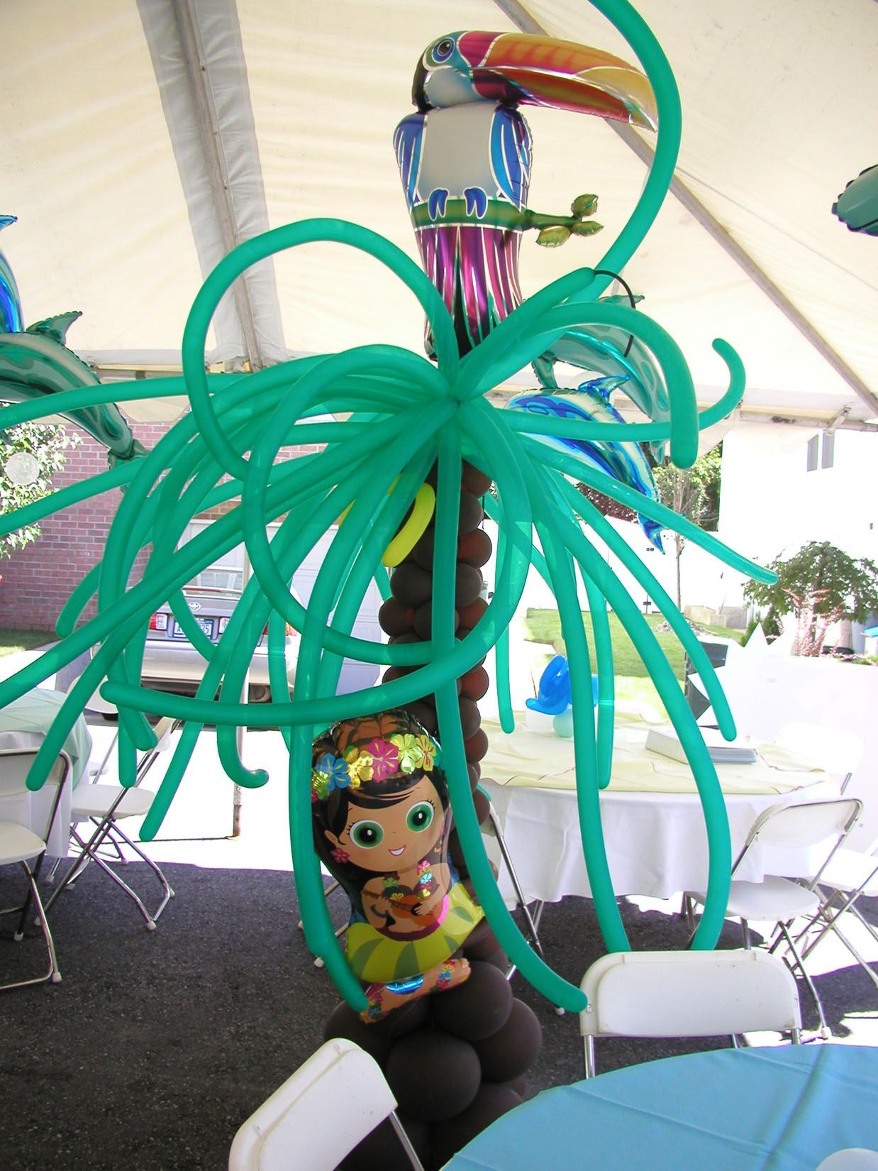 Balloon palm tree with a toucan, hula girl, and green fronds, set at a party.
