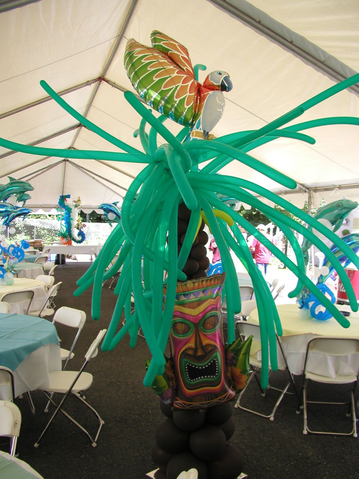 Balloon sculpture: Tiki totem pole with parrot, palm fronds, black and green balloons, set inside a tent.