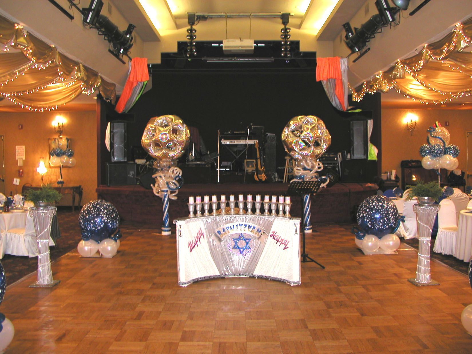 Hanukkah celebration with stage, menorah, balloons, and decorated tables.