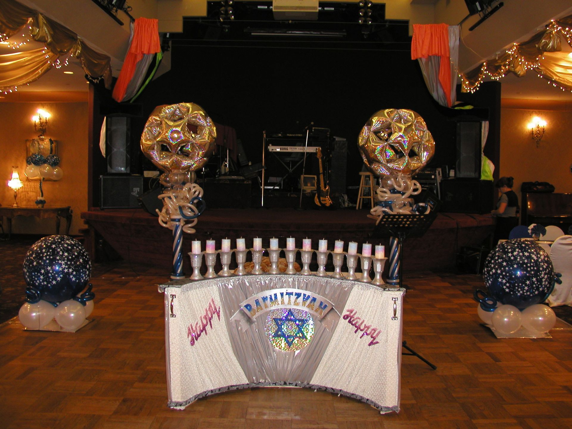 Bar Mitzvah stage decorated with balloons, menorah, and banner, in a ballroom.