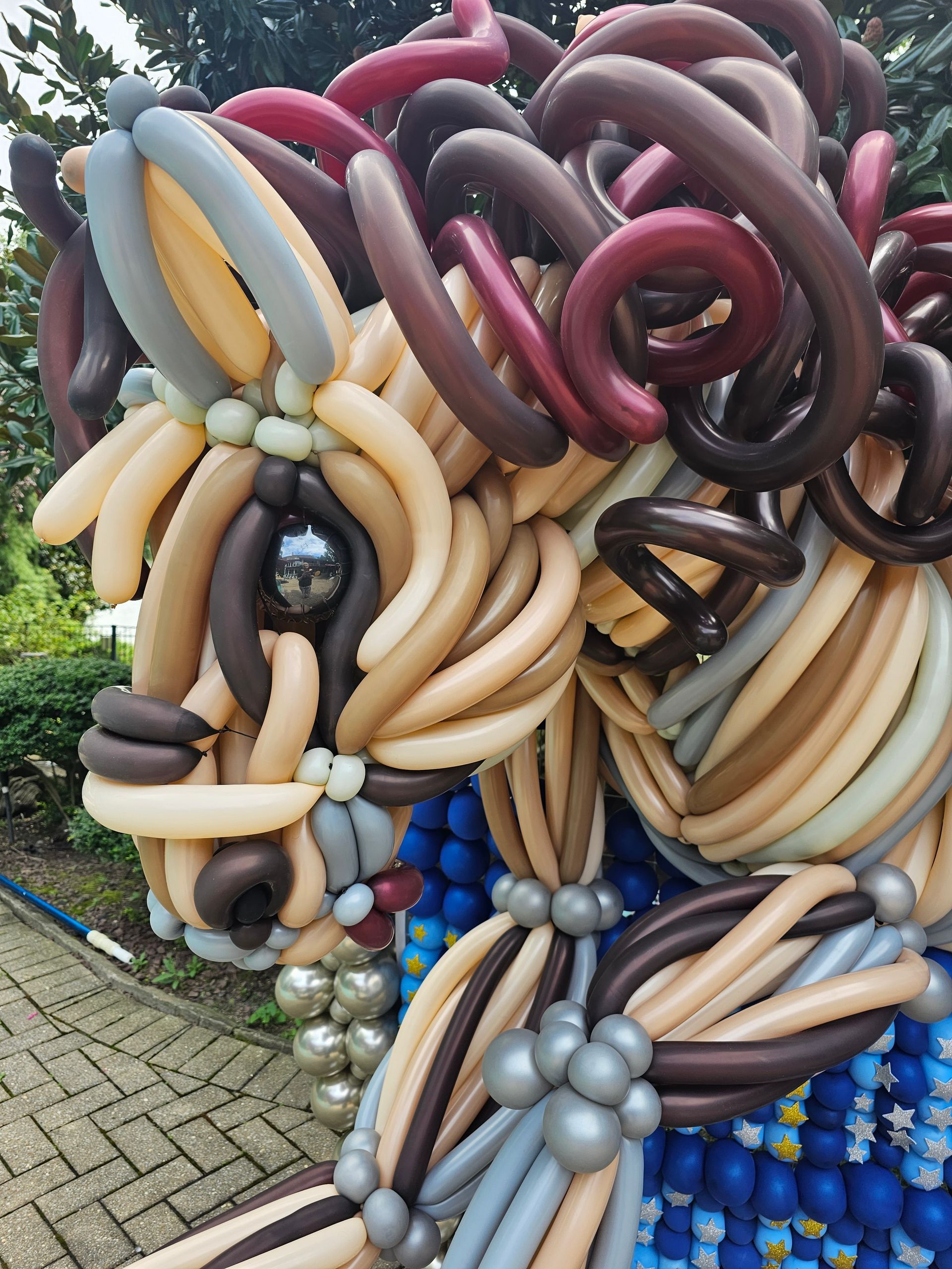 Balloon sculpture of a horse with tan, brown, and grey balloons; outdoors.