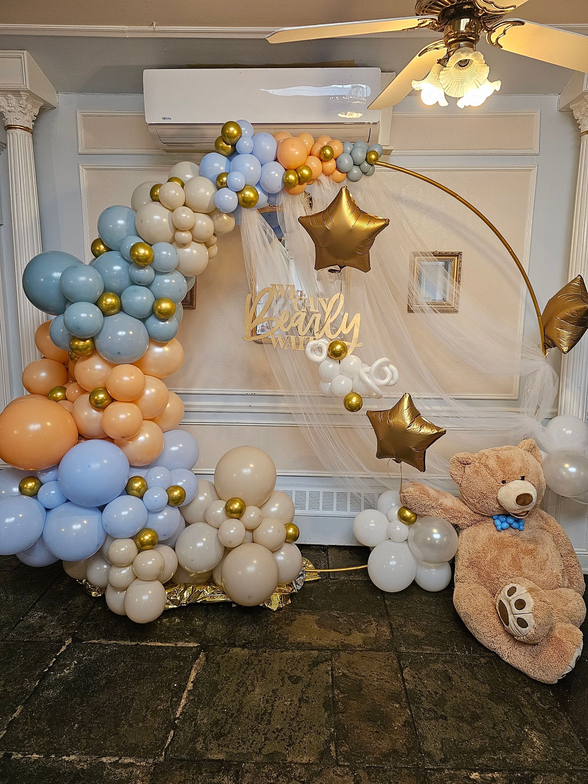 Balloon arch and teddy bear decorations for a baby shower. Pastel colors, gold accents, and a 