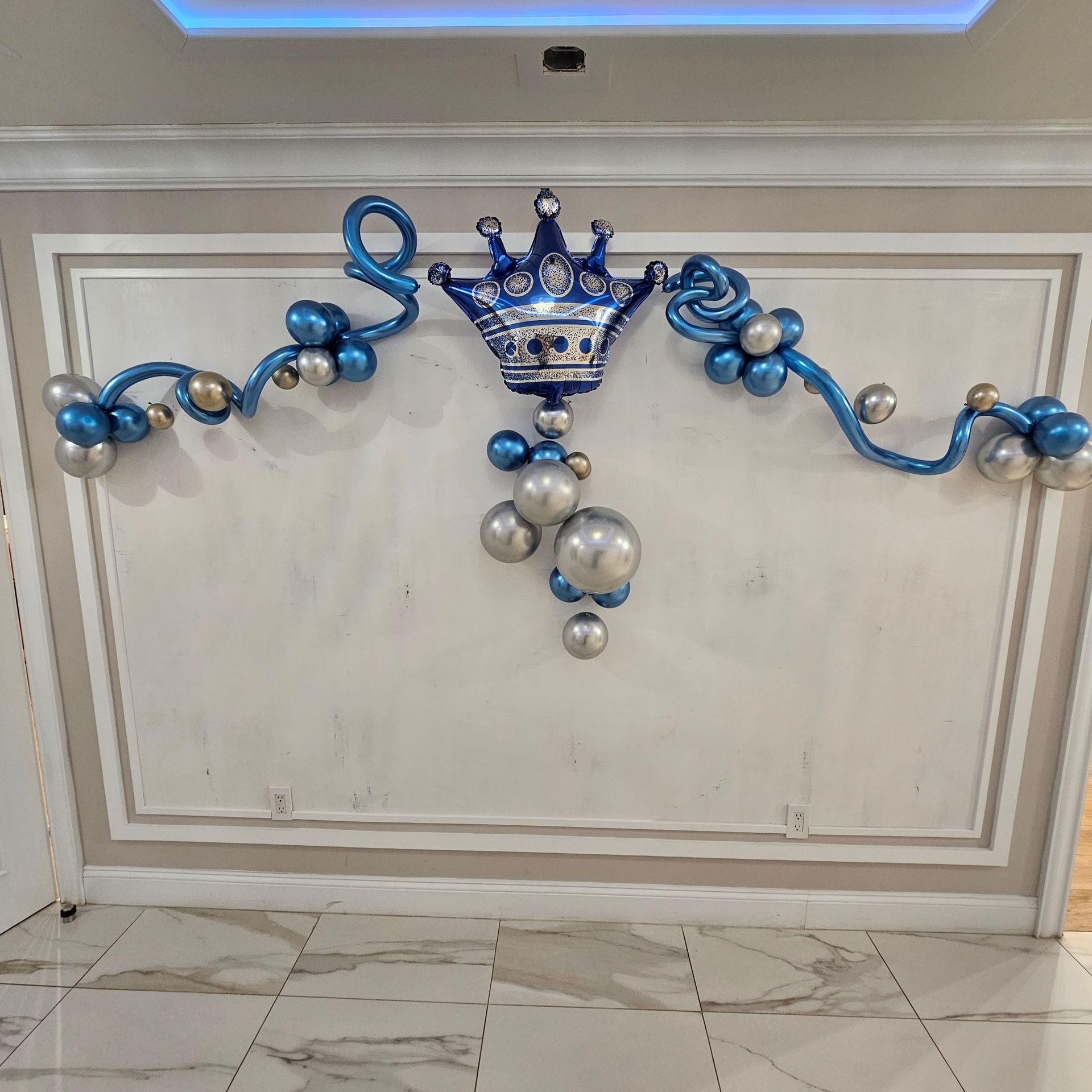Blue and silver balloon crown and garland decorates a wall.