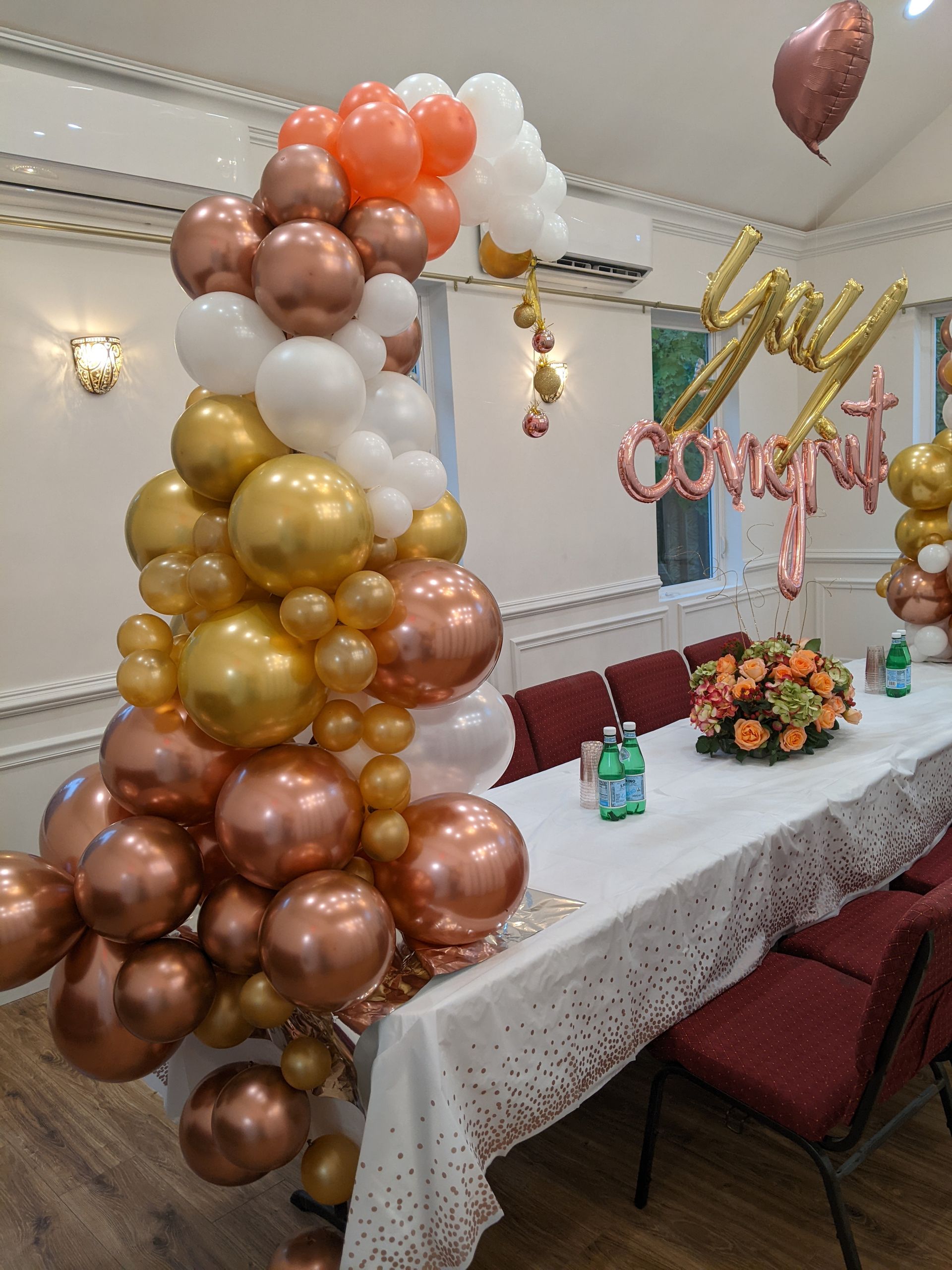 Balloon arrangement with copper, gold, white, and orange balloons. Table set for celebration, 