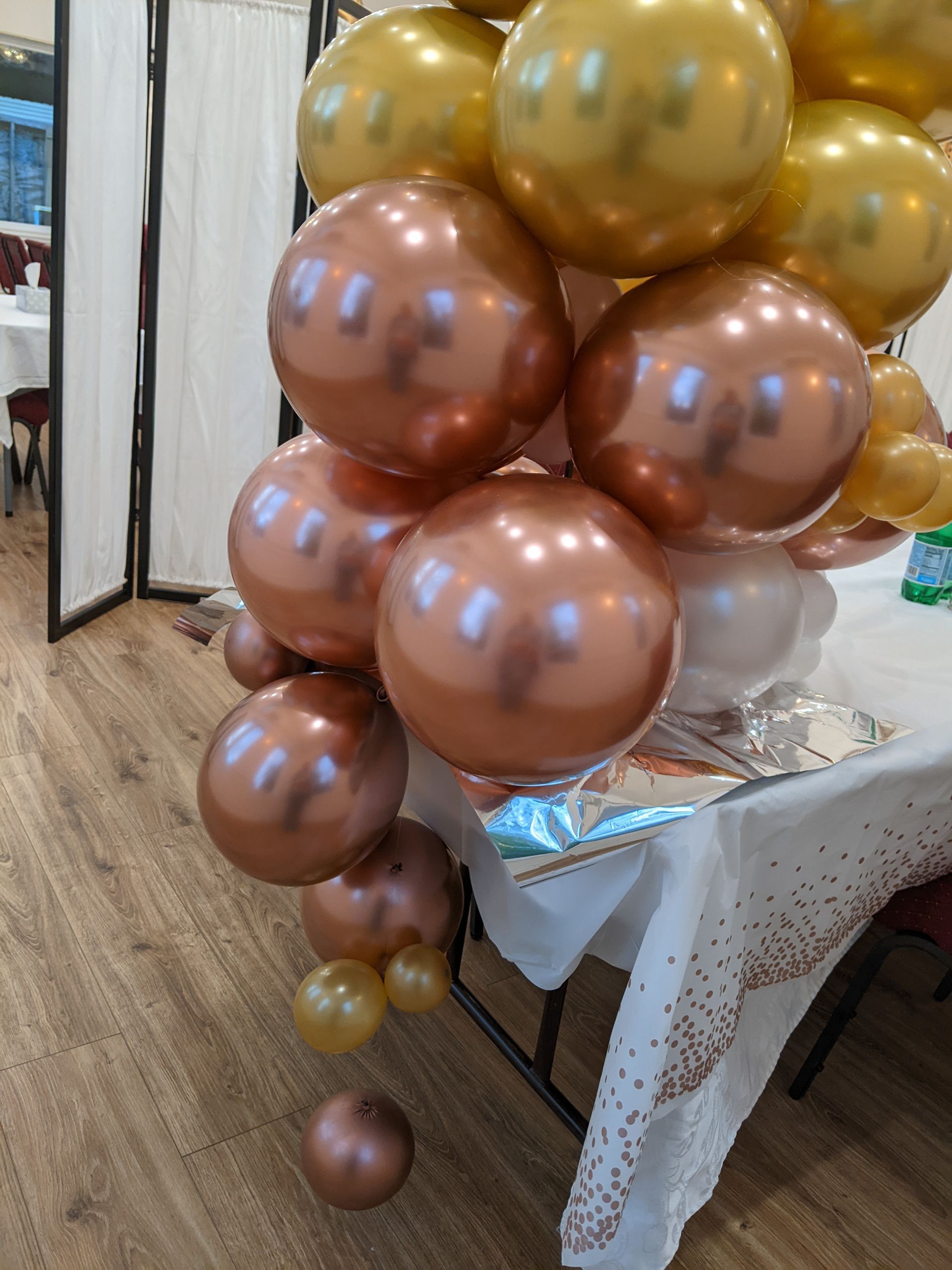 A cluster of gold and bronze balloons on a table covered with a white tablecloth.