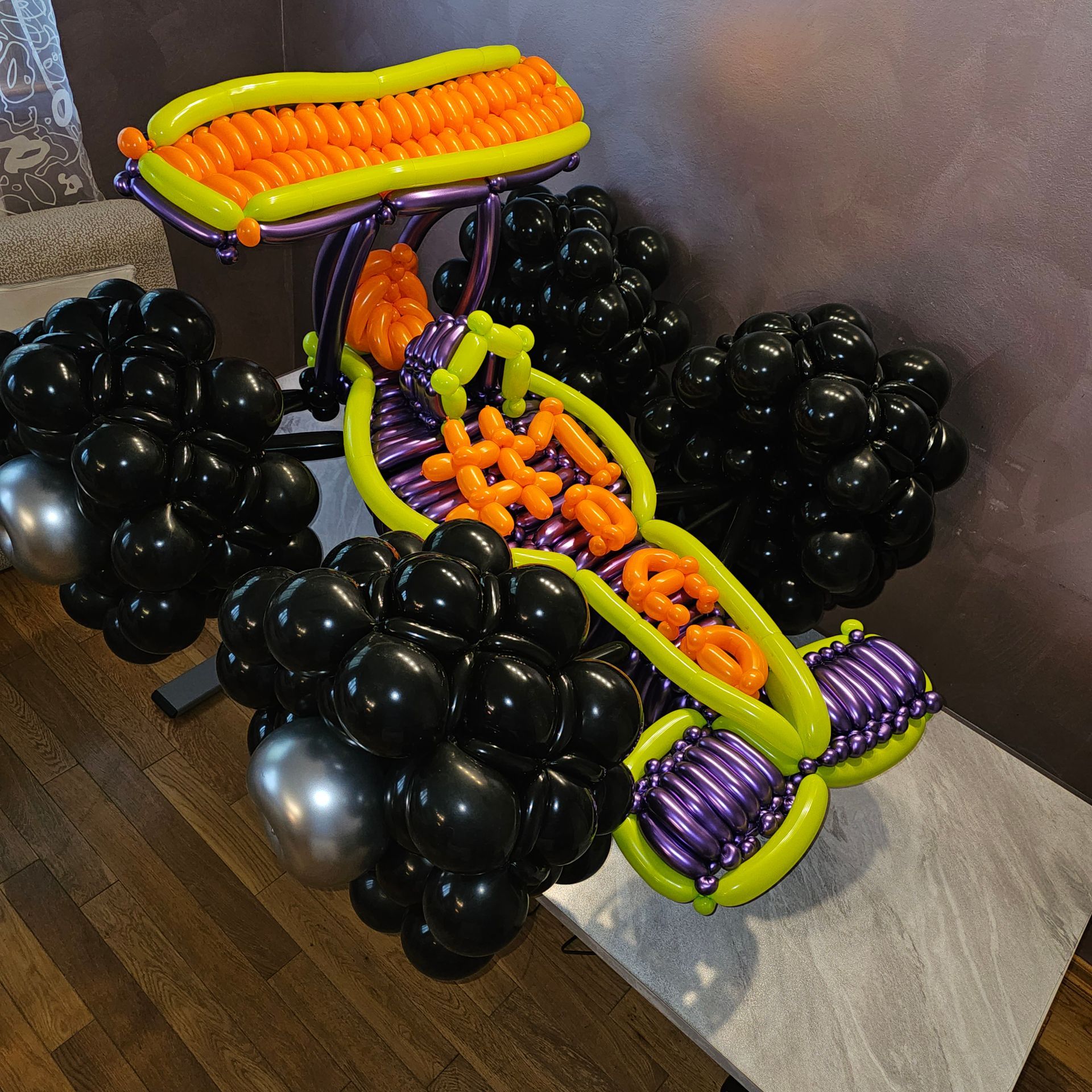 A balloon sculpture of a Halloween-themed monster truck; orange, black, purple, yellow balloons.