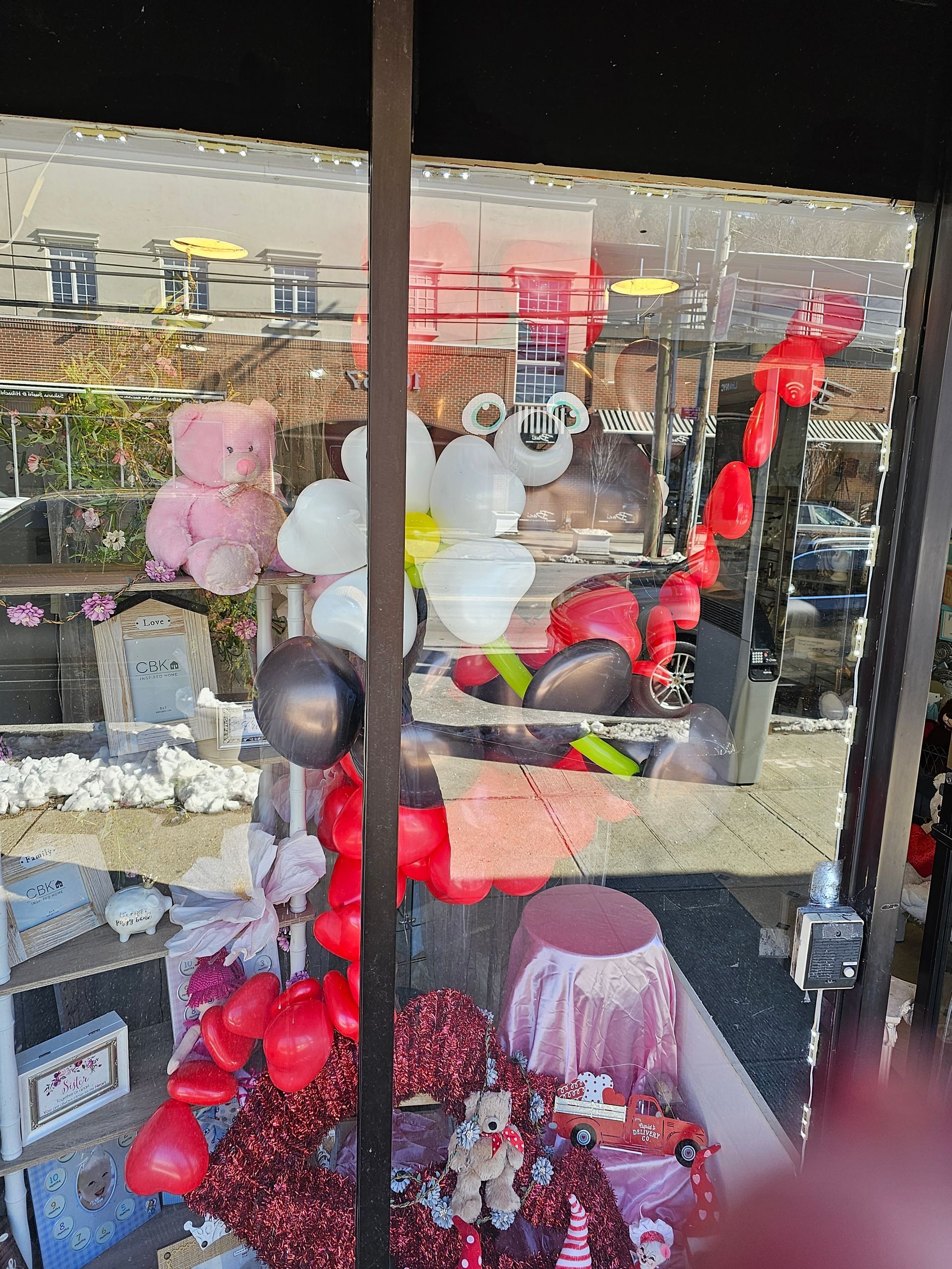 Shop window display with balloons, teddy bears, and red decorations.