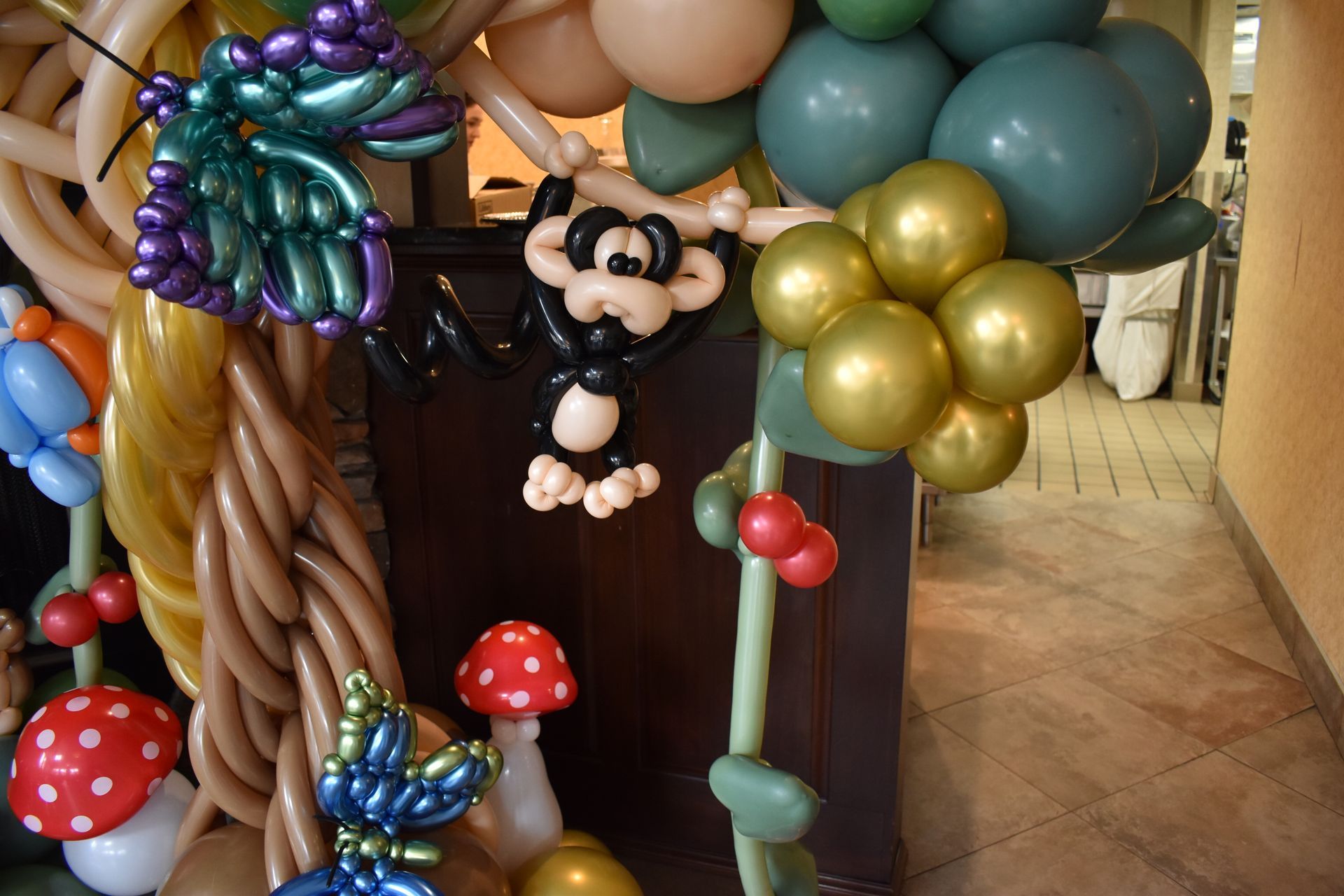 Balloon sculpture with monkey, mushrooms, foliage, and balloons in various colors.
