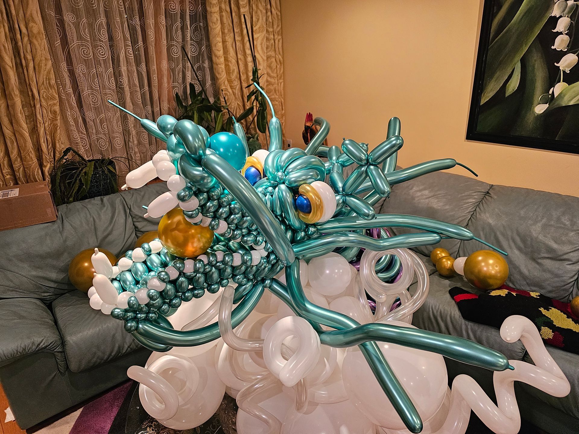 A teal and white balloon dragon sculpture with gold accents on a couch.