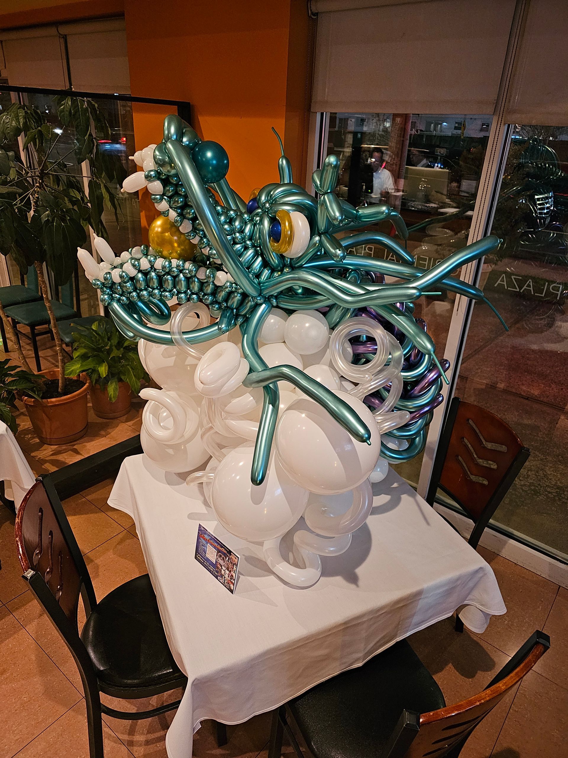 A teal and white balloon dragon sculpture on a white tablecloth in a restaurant.
