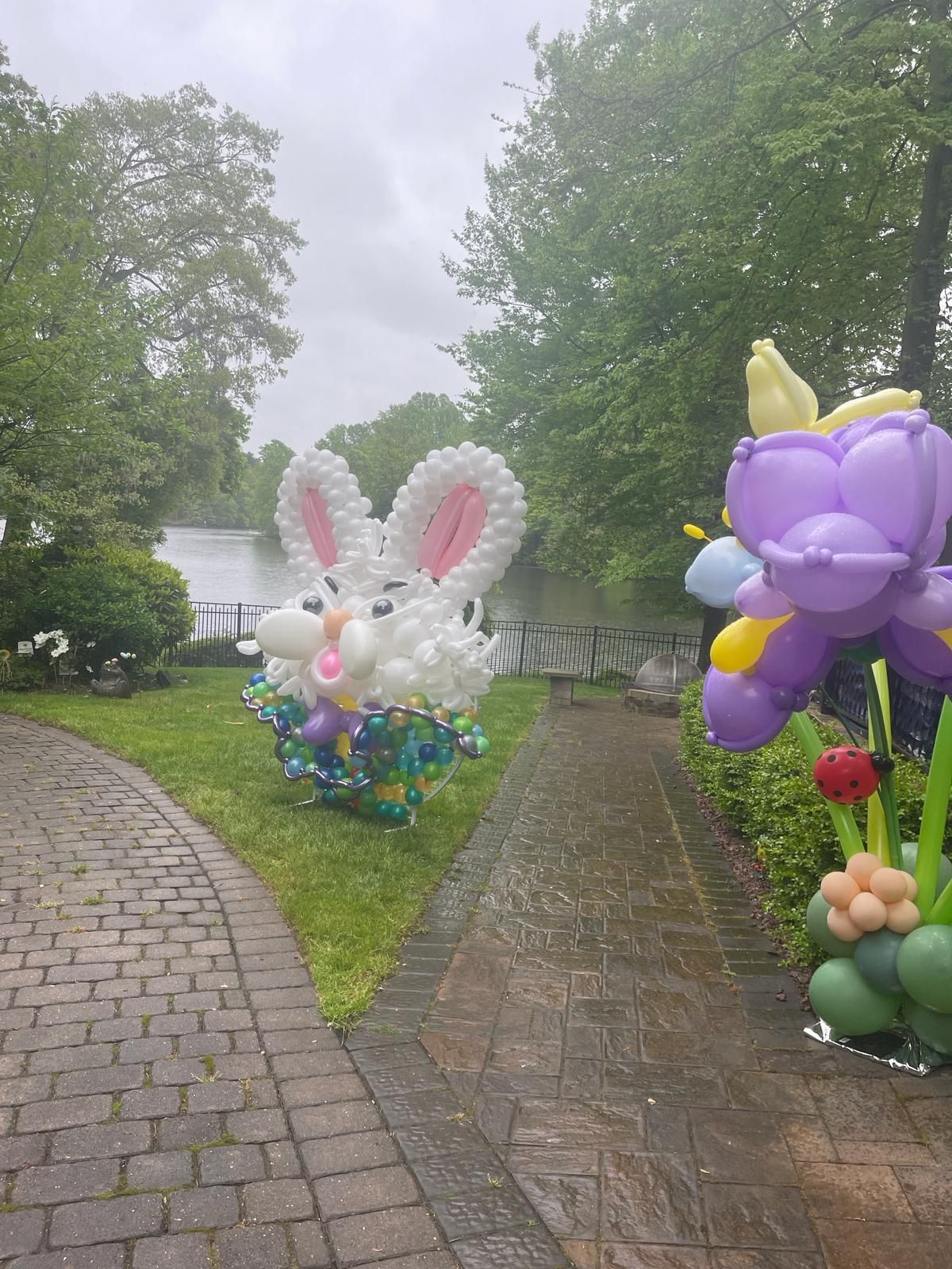 Balloon sculpture of a white Easter bunny and purple flower in an outdoor setting with a lake in the background.