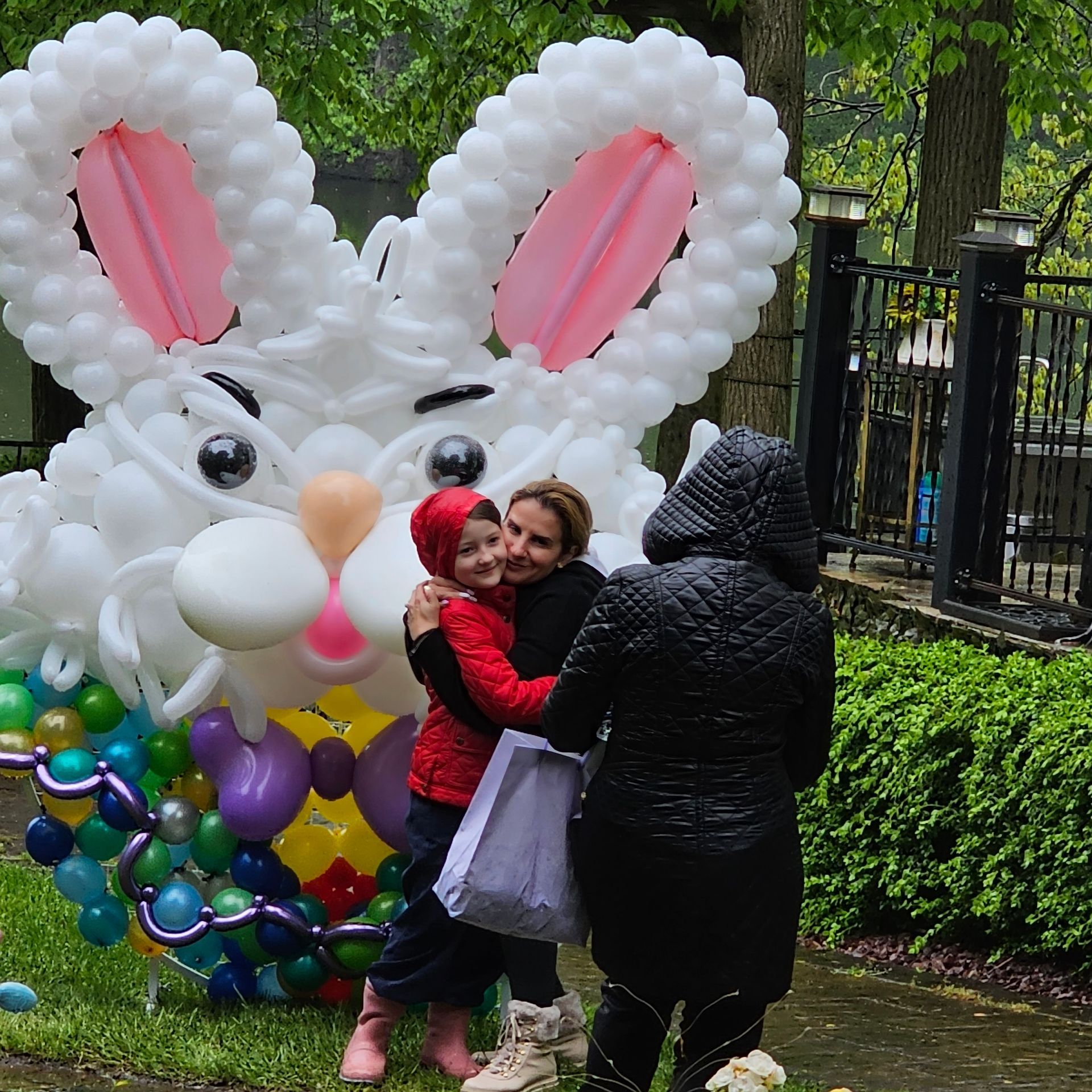 People hugging in front of a giant balloon bunny sculpture with colorful egg basket.