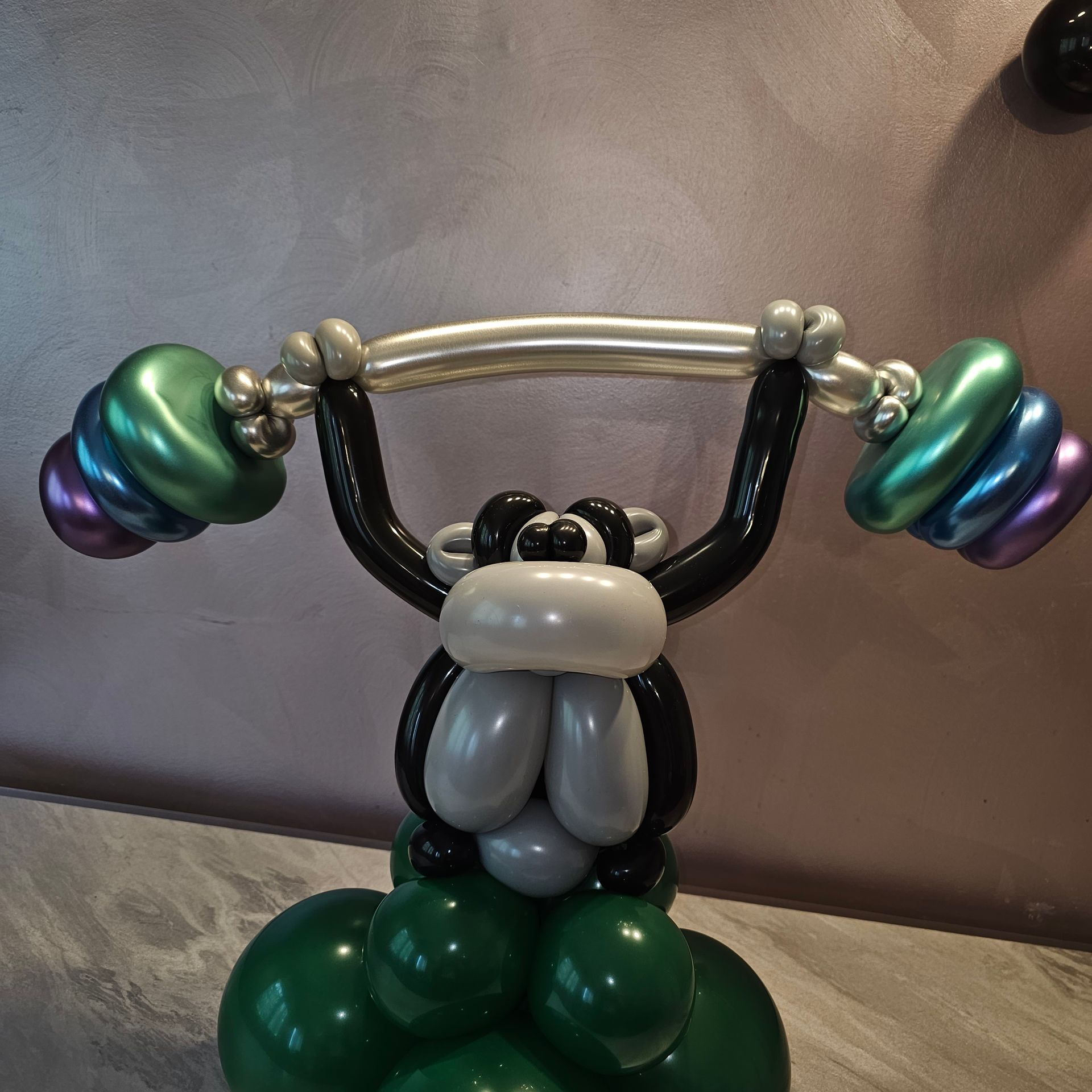 Balloon sculpture of a monkey lifting weights, composed of colorful balloons.
