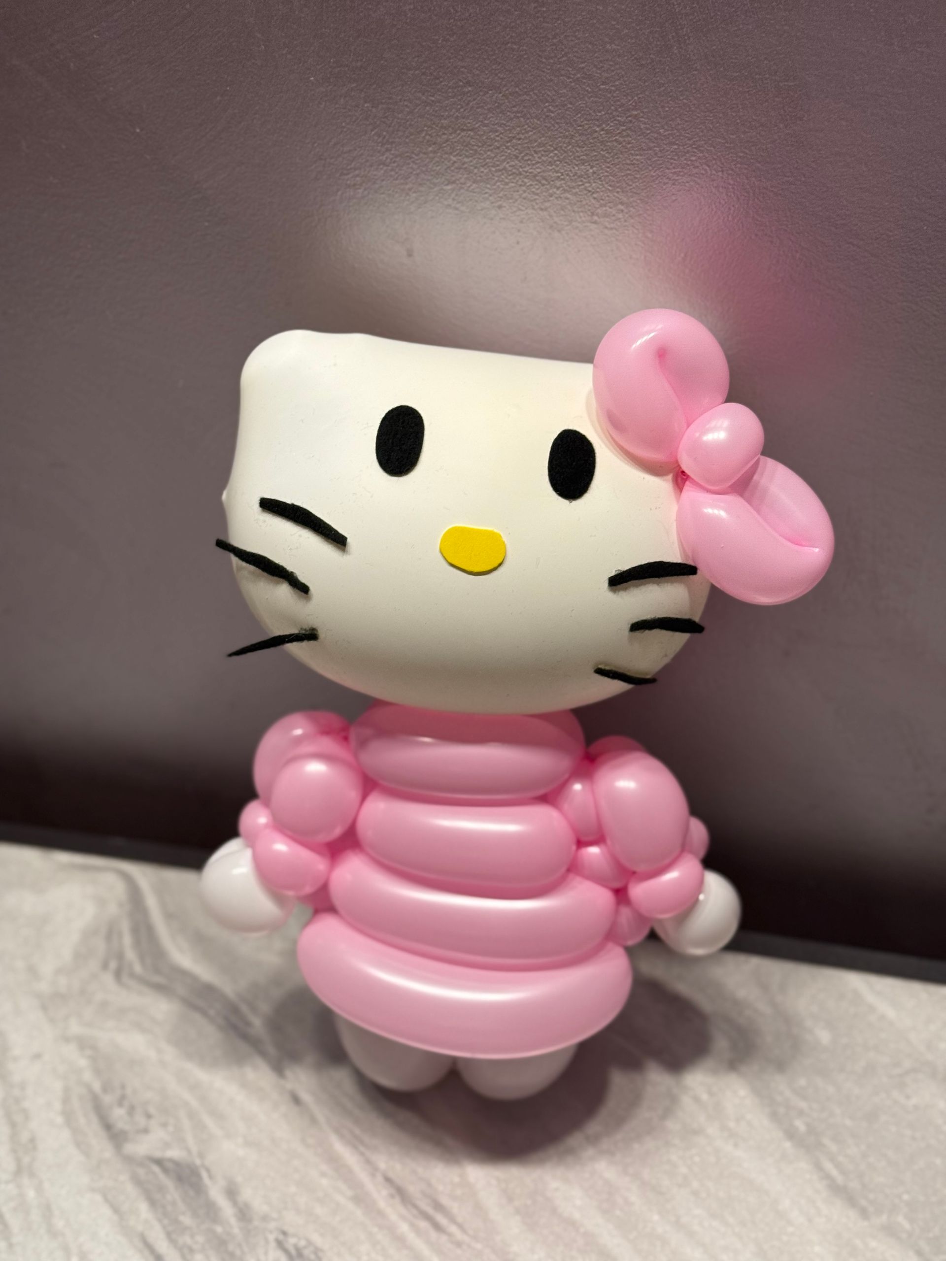 Hello Kitty balloon sculpture, white head with black eyes and whiskers, pink bow and dress.