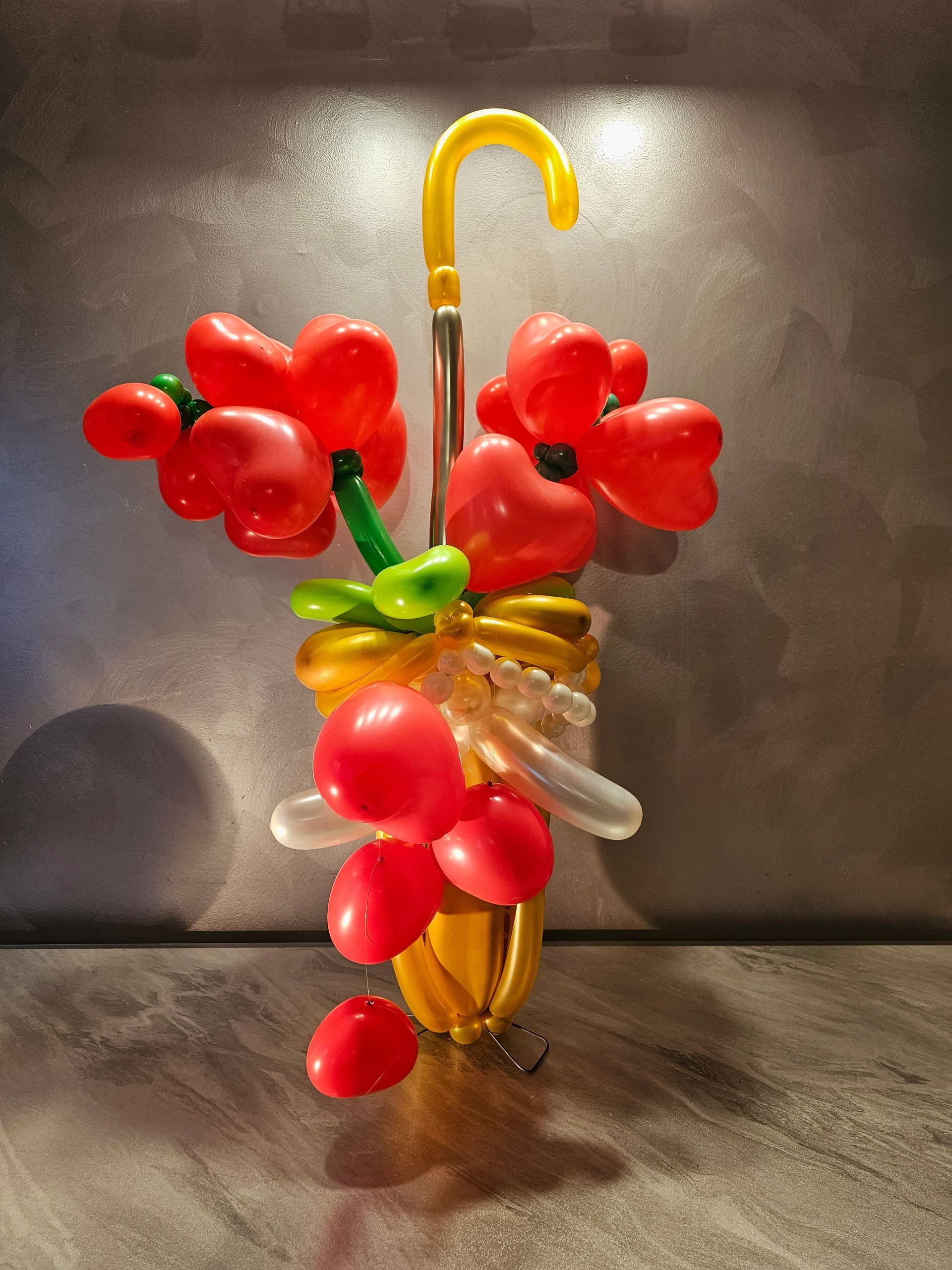 Balloon sculpture of a yellow umbrella holding red heart-shaped flowers.