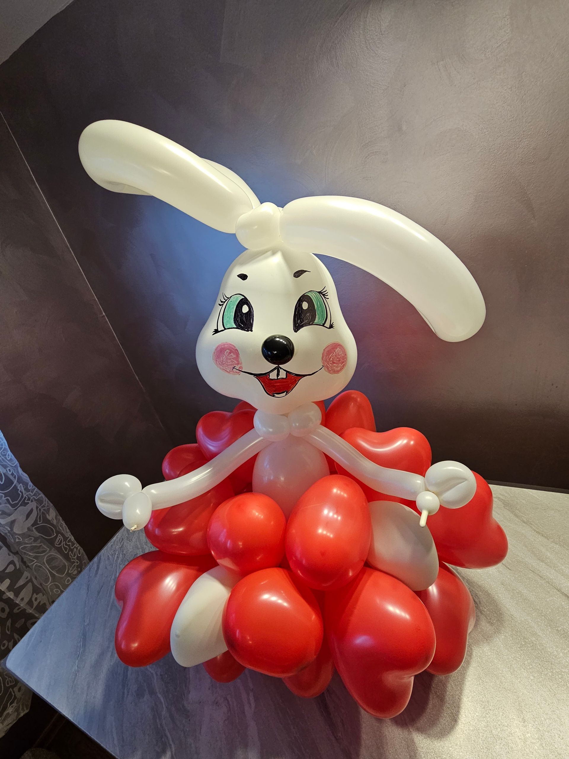 Balloon bunny sculpture with red heart-shaped body, white head, ears, and arms, sitting on a surface.