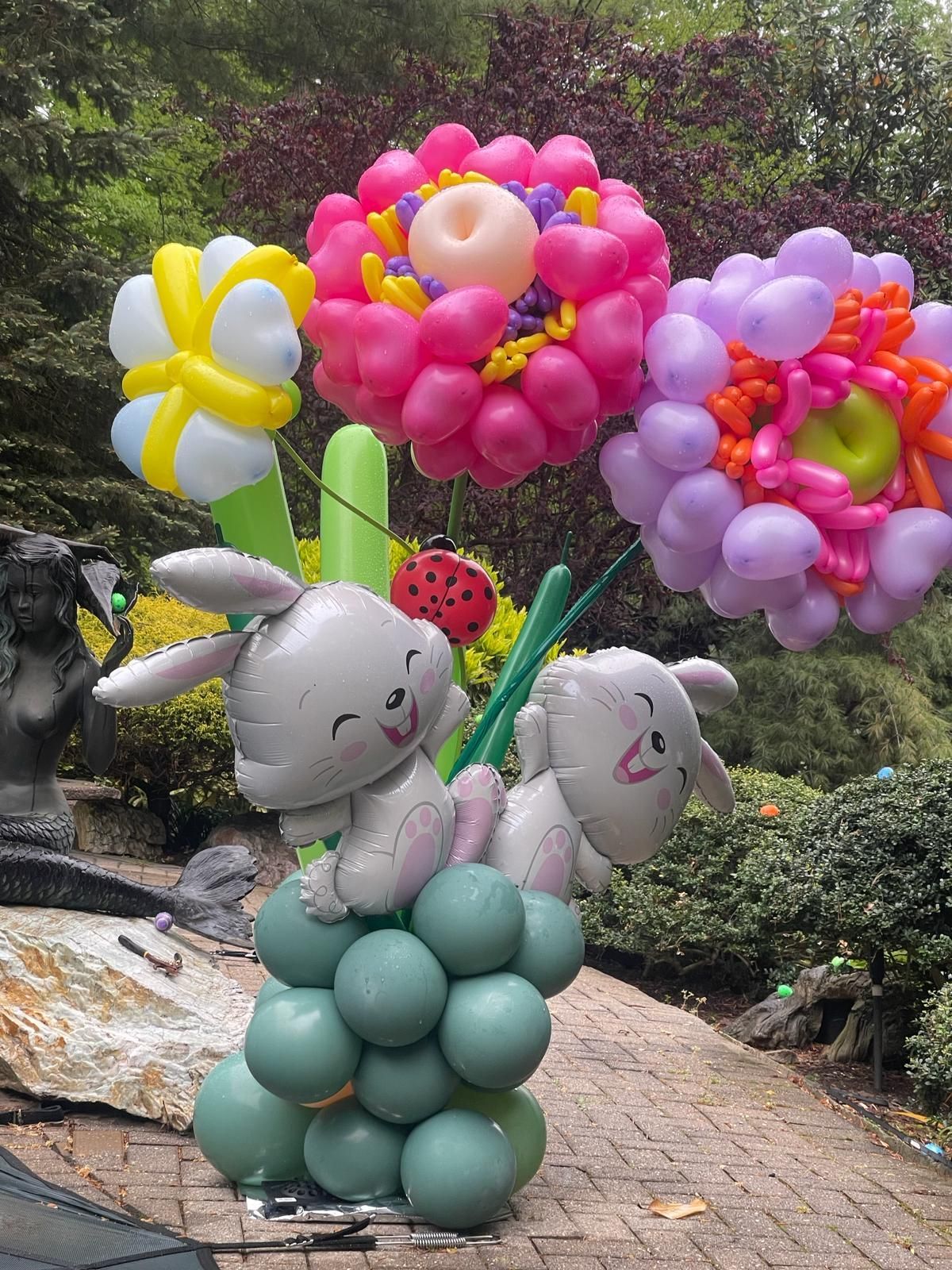Balloon sculpture of bunnies and colorful flowers outdoors.