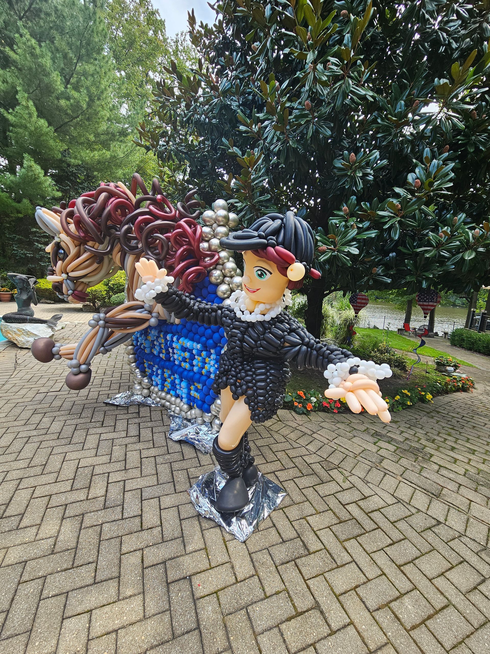 Sculpture of a person on a horse, both made of balloons, on a brick path, with trees in the background.