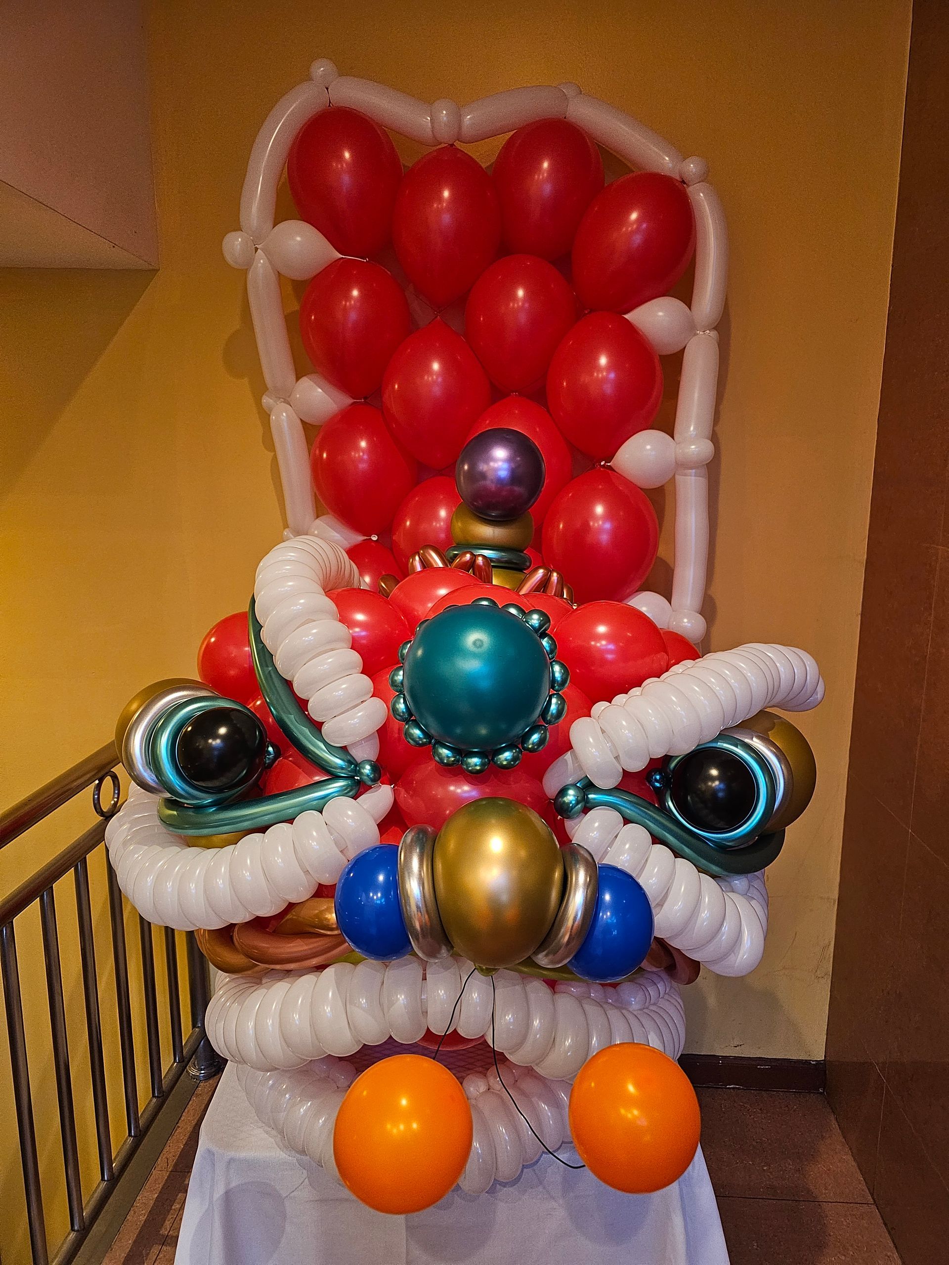 Balloon sculpture of a Chinese dragon head in red, white, and gold, with orange accents.