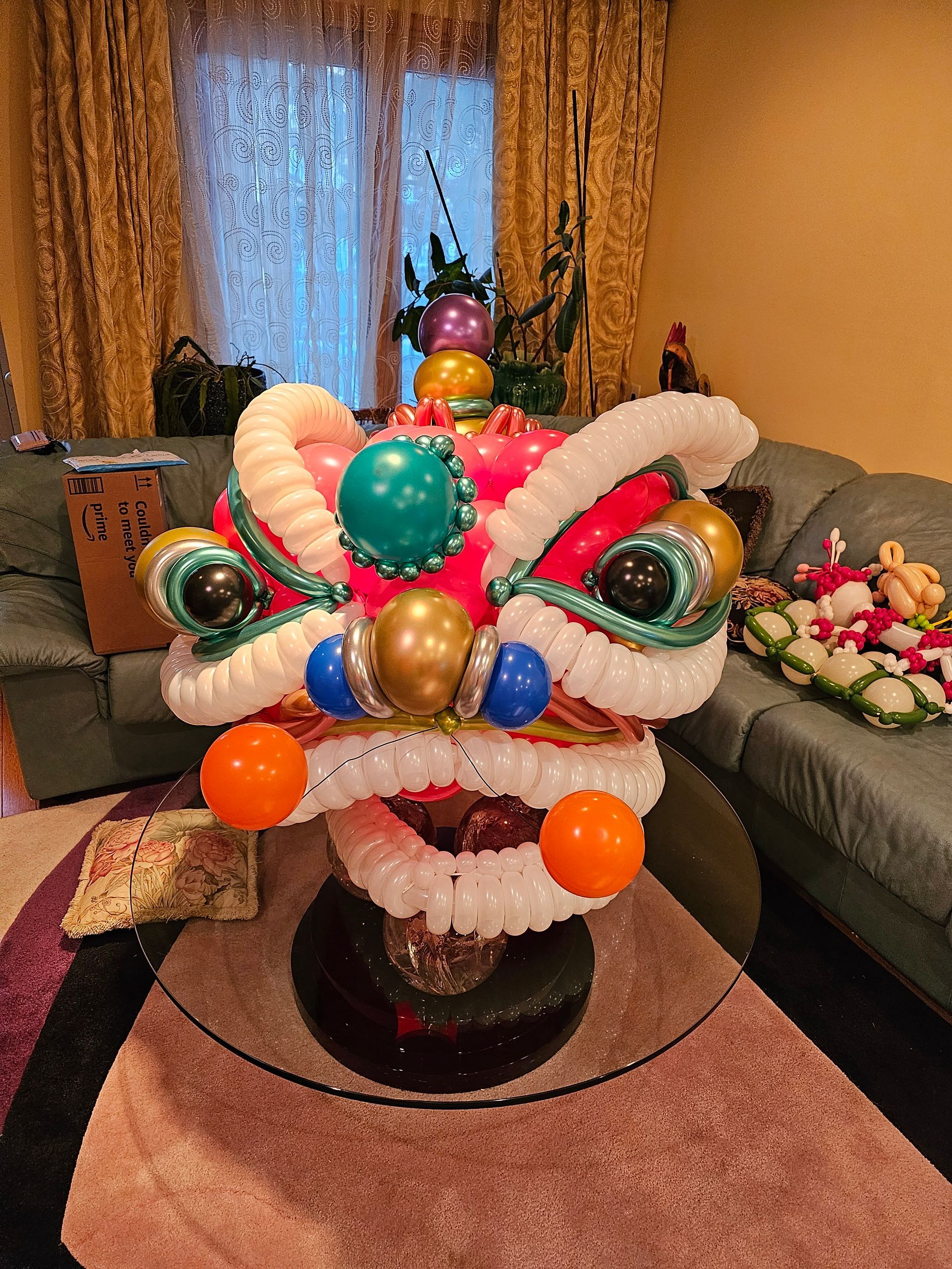 Balloon lion head sculpture on a table, colorful with red, white, and gold accents, indoors.