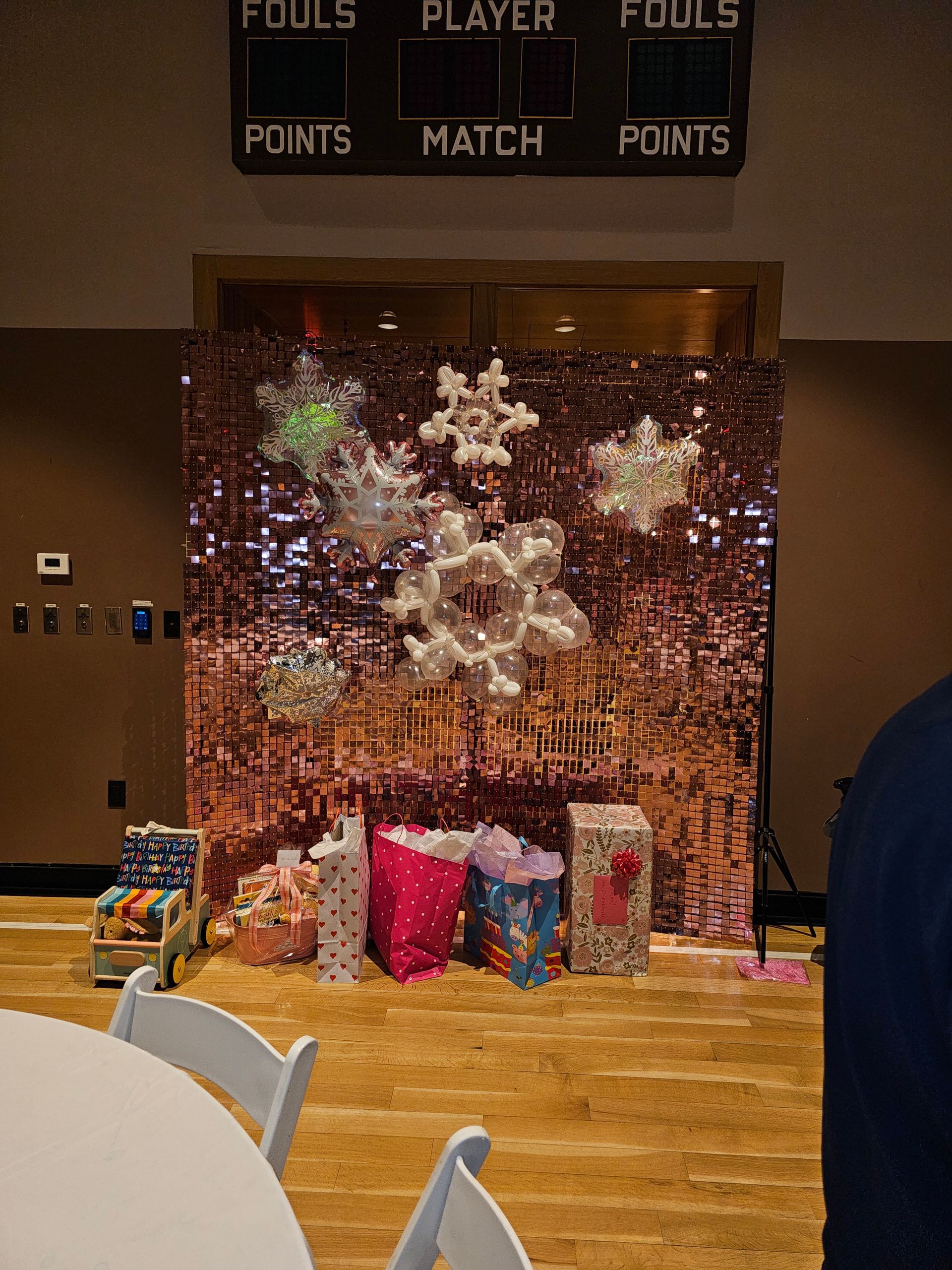 Photo booth with a rose gold sequin backdrop, snowflake decorations, and gifts.