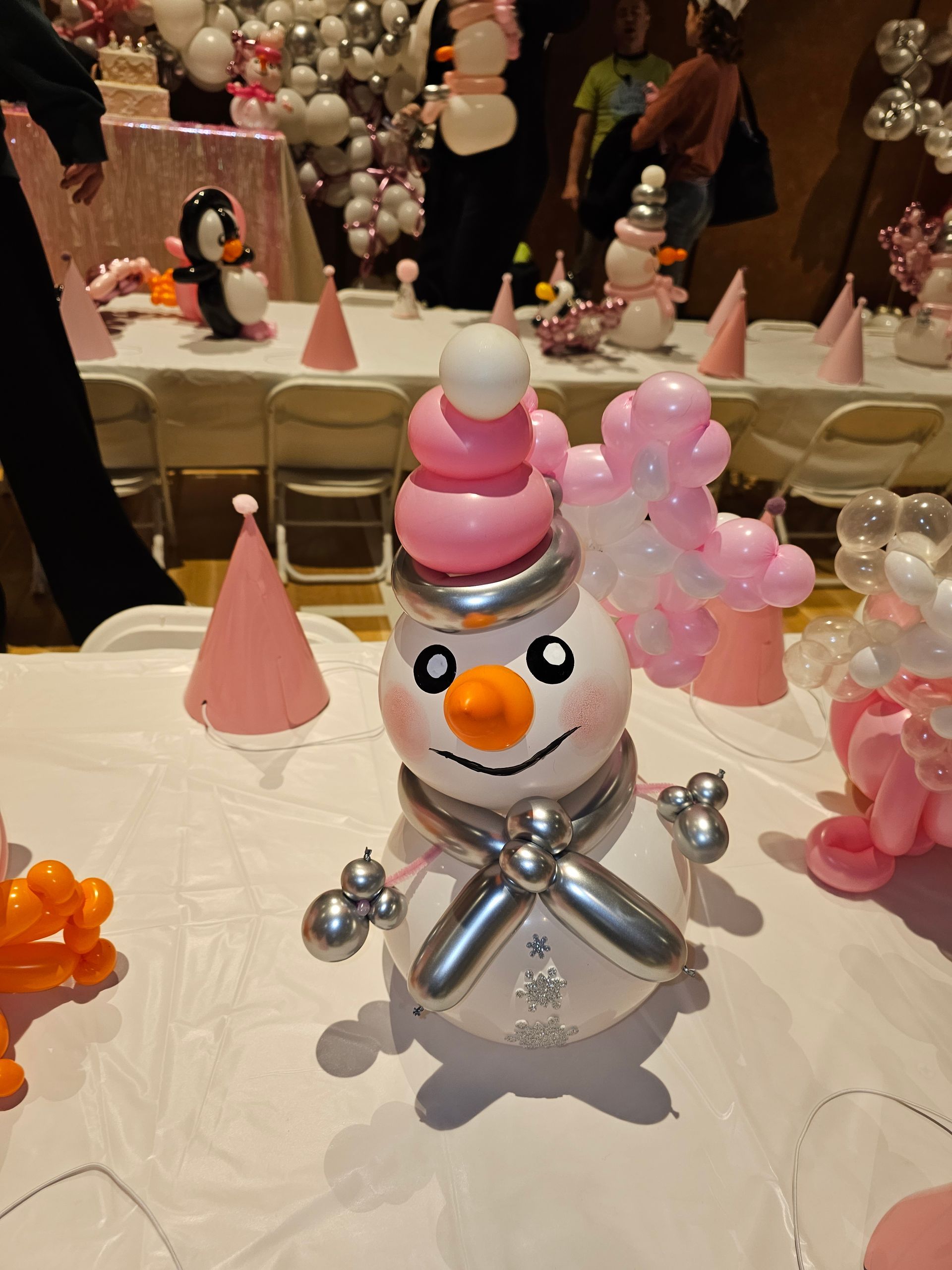 A balloon snowman centerpiece at a pink-themed party, with other balloon decorations and a long table.
