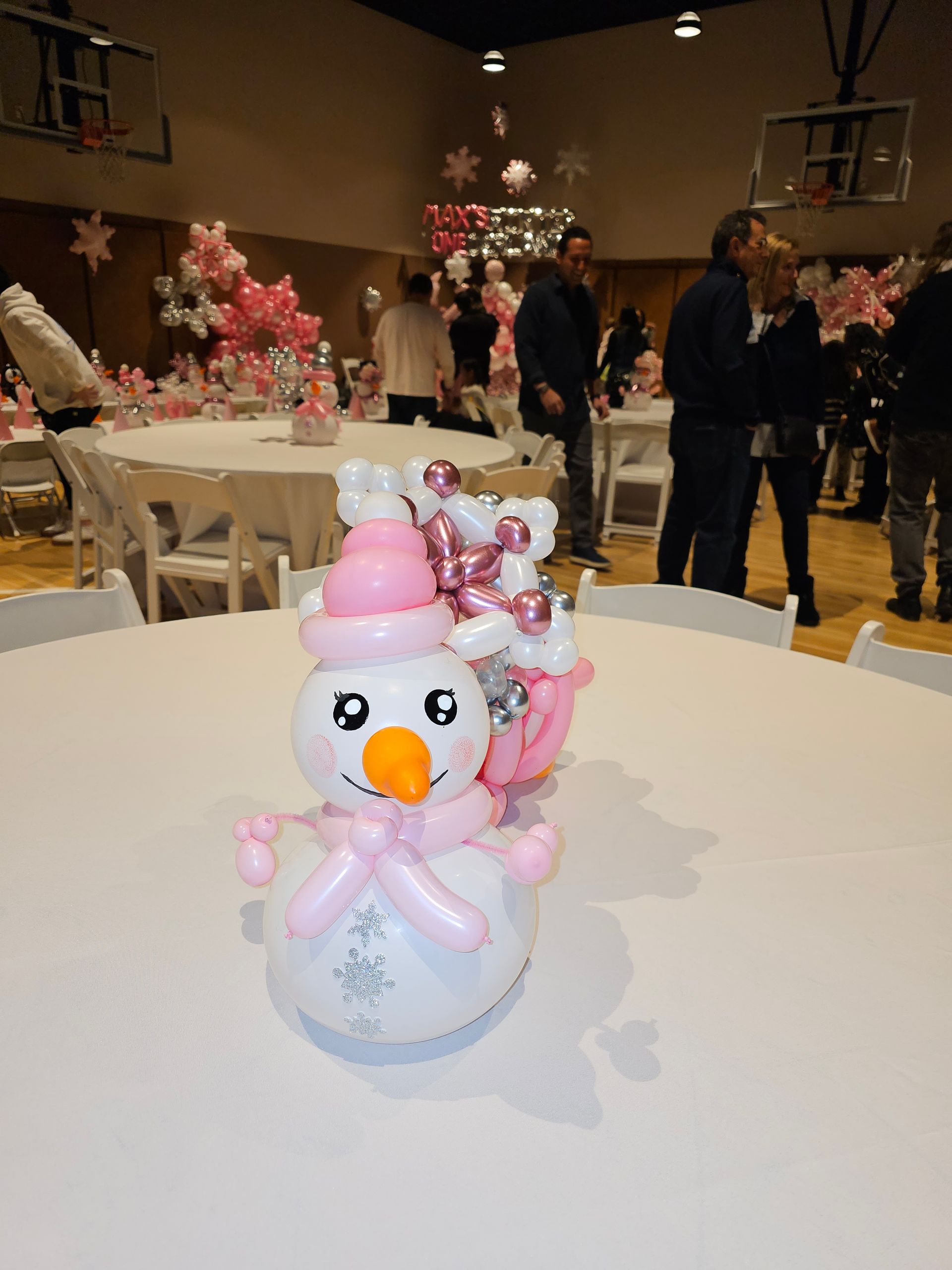 Balloon snowman centerpiece with pink and white decorations at an event. People and tables in background.