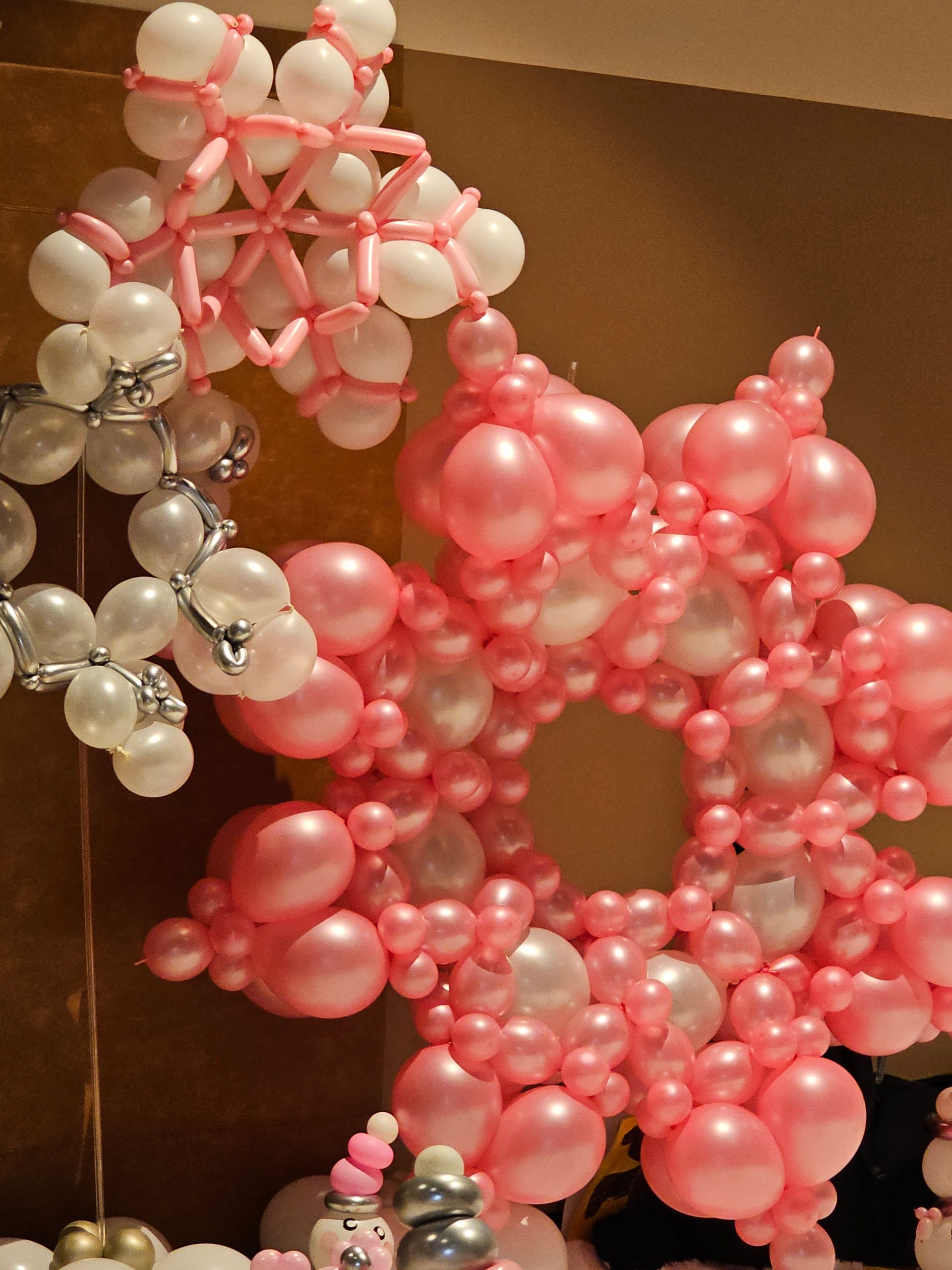 Pink and white balloon sculpture in the shape of a snowflake, indoor setting.
