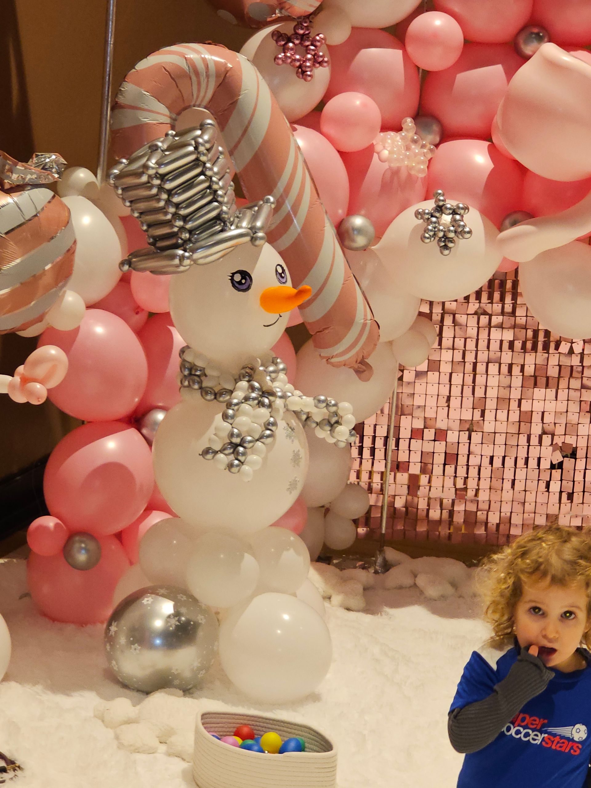 Snowman balloon sculpture with pink and white balloons, child looking on.