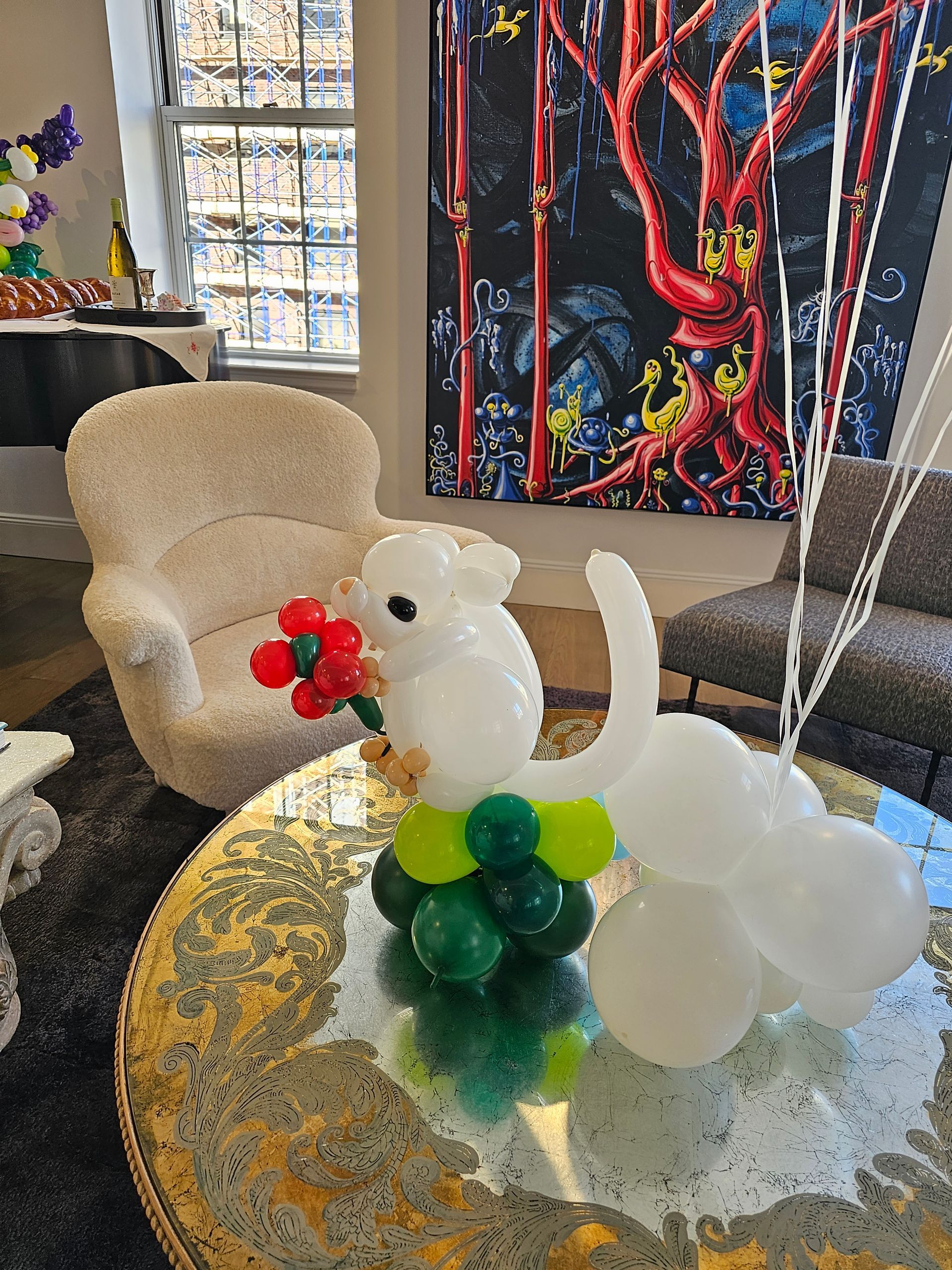 Balloon sculpture of a white mouse holding a flower, on a gold table.