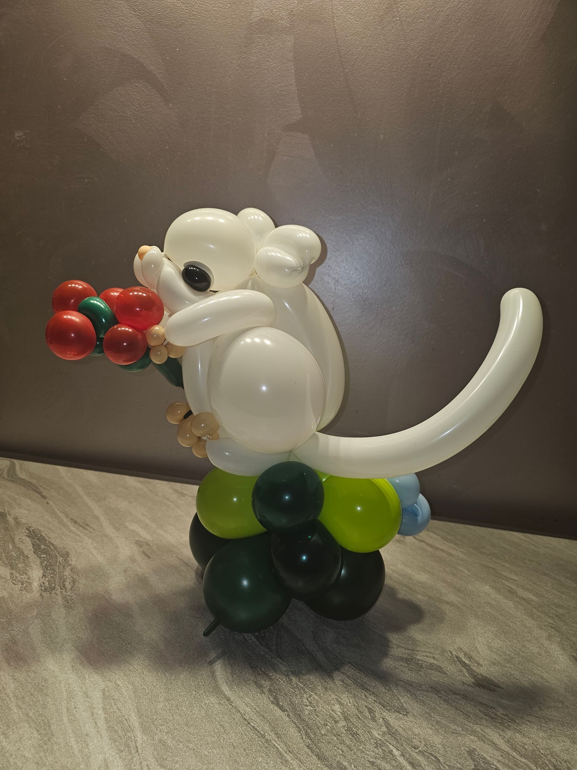 White balloon monkey sculpture holding red balloon flowers, on a gray surface.