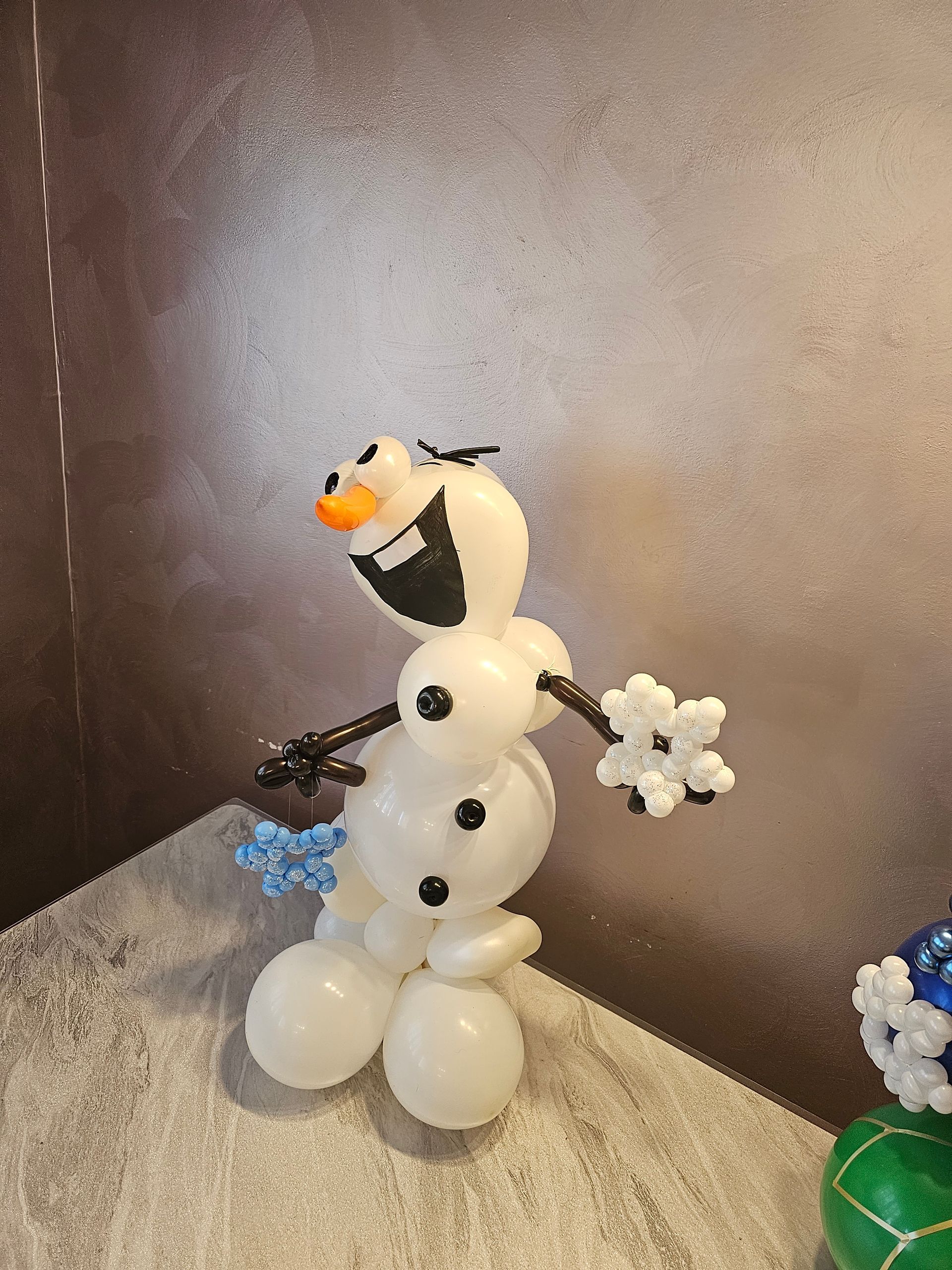 Olaf the snowman made of white balloons, with snowflake arms, against a textured background.
