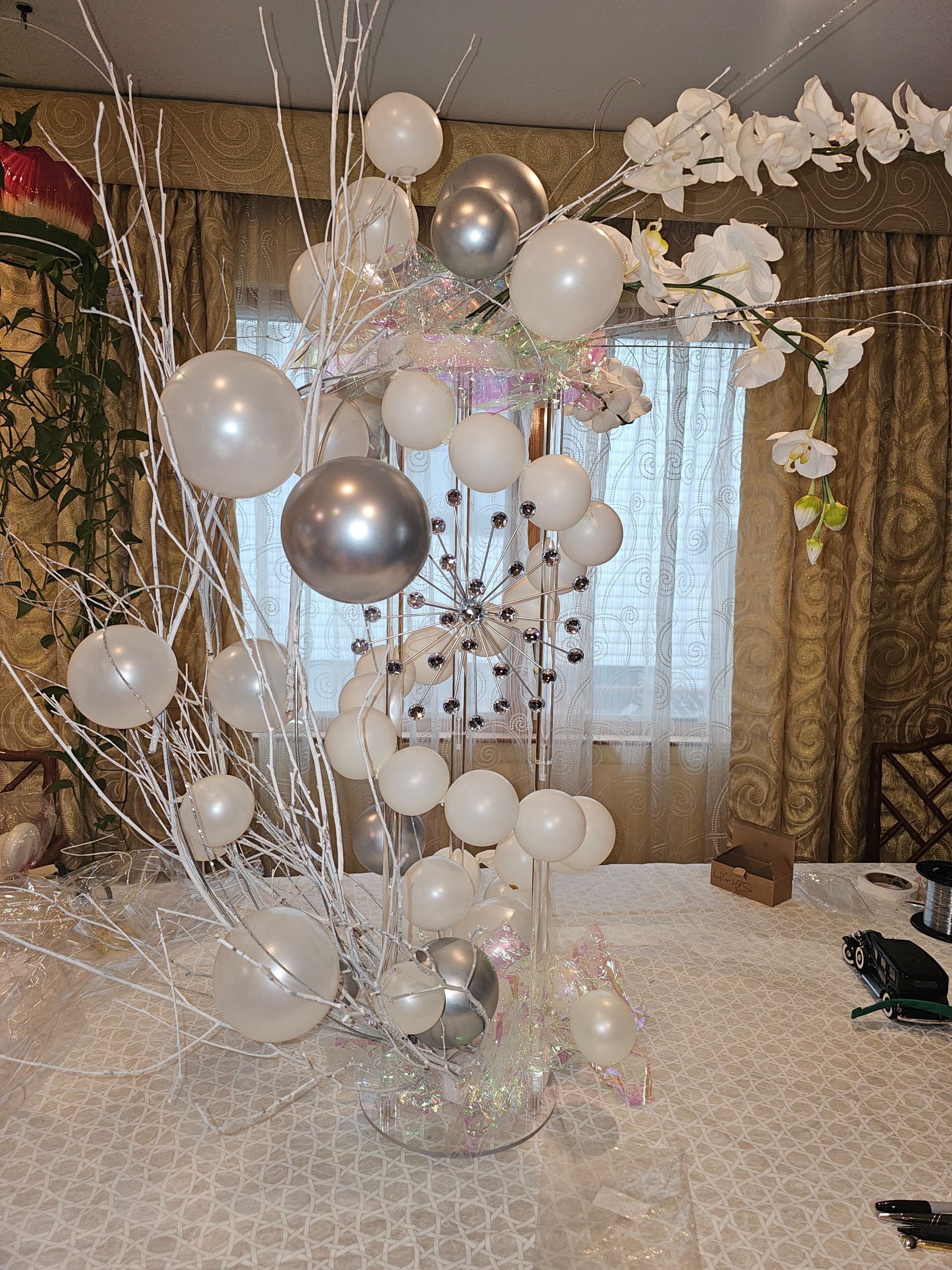 Centerpiece with silver and white balloons, branches, and floral accents on a table.