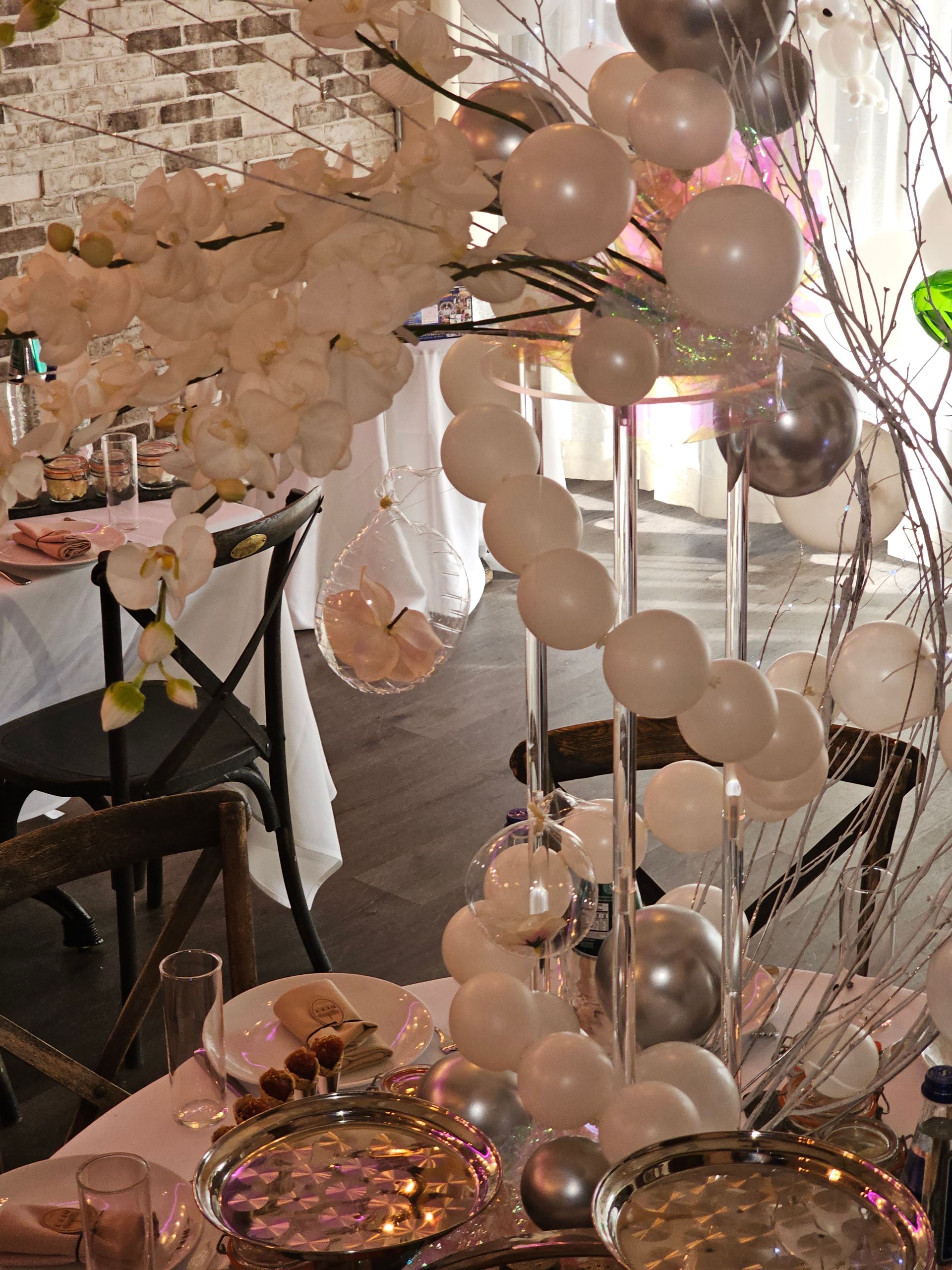 Table setting with white and silver balloons, floral arrangements, and glass decorations.