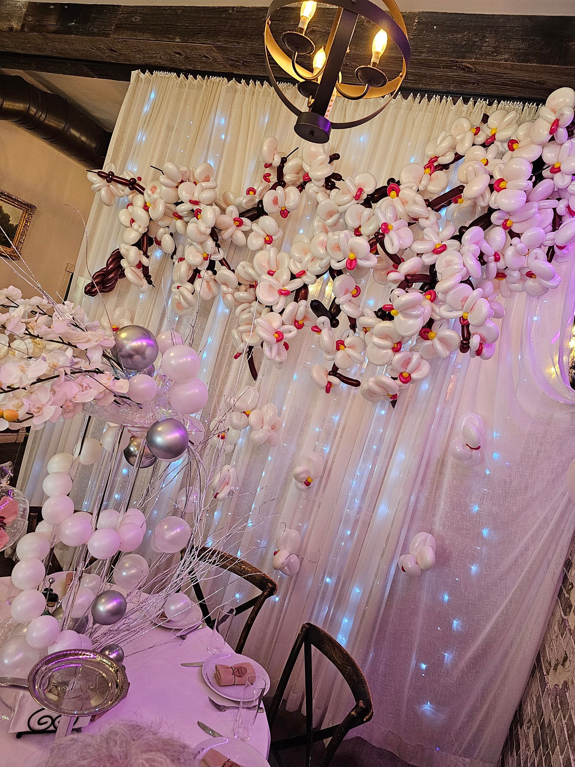 White floral arrangement on a sparkly backdrop with balloons.