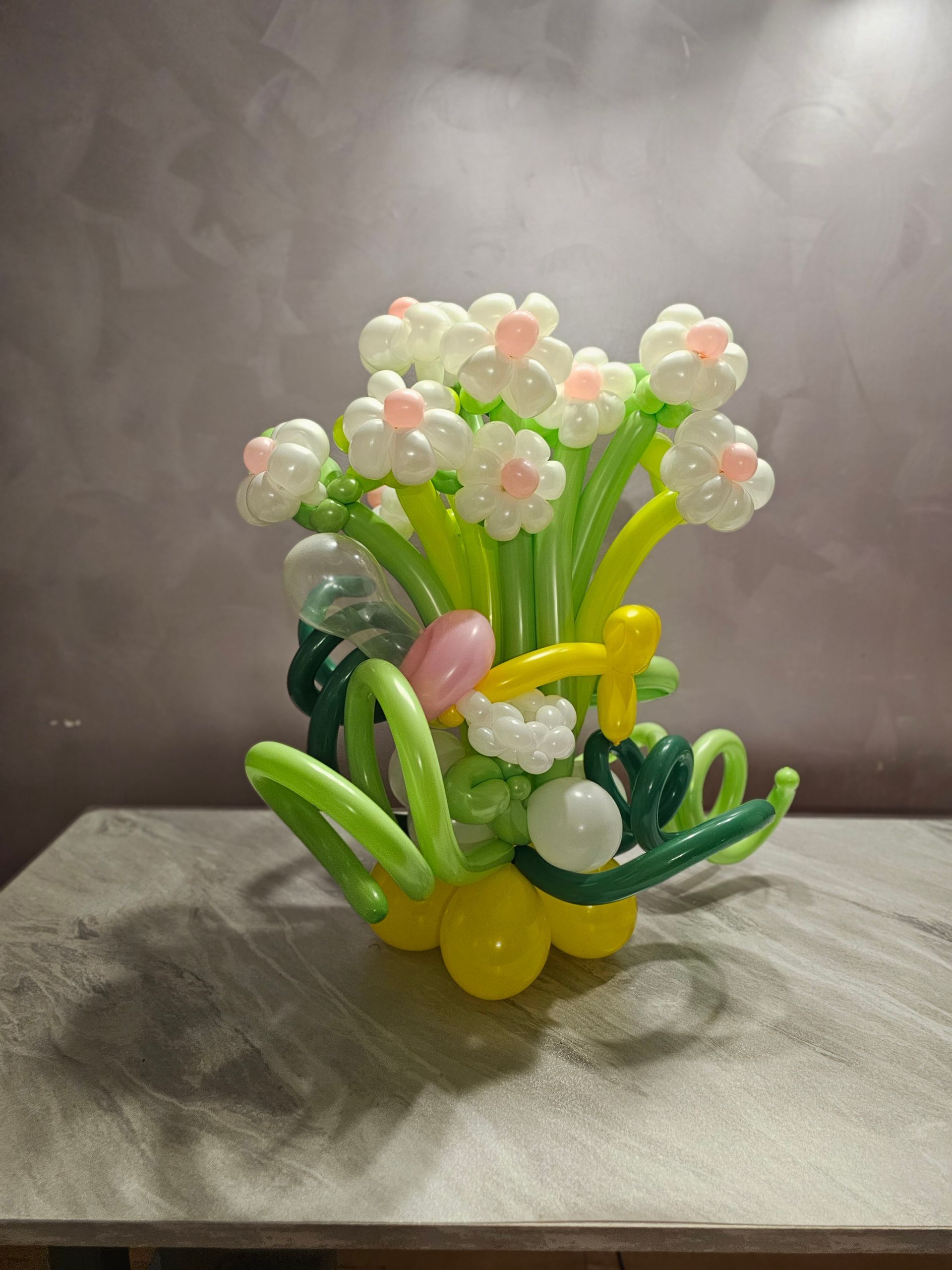 Balloon sculpture of a flower bouquet with white and pink blossoms, green stems, and a yellow base.