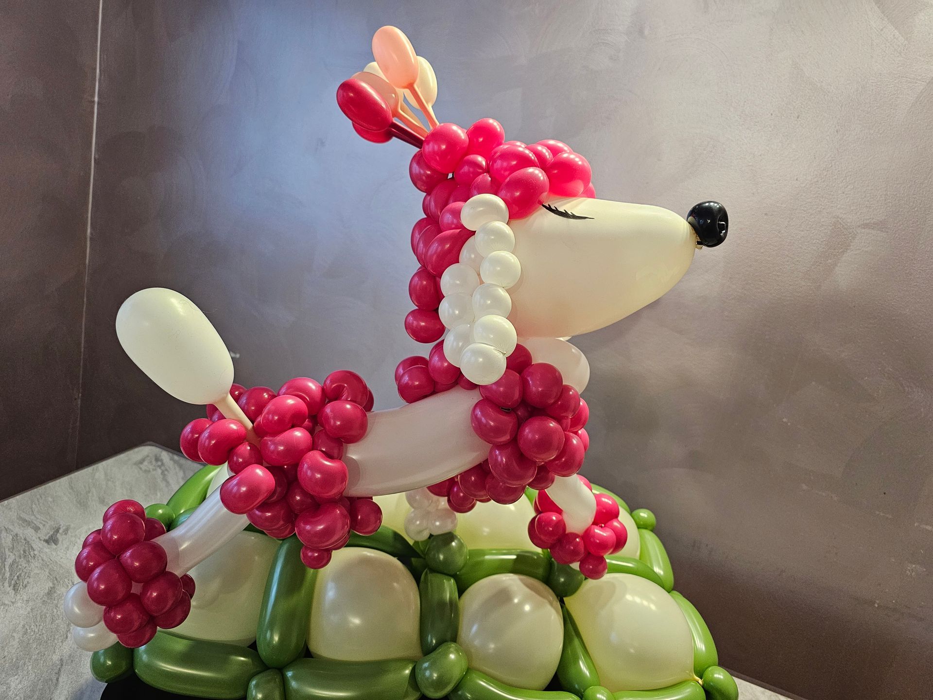 Balloon poodle sculpture, white and pink, with a green base.