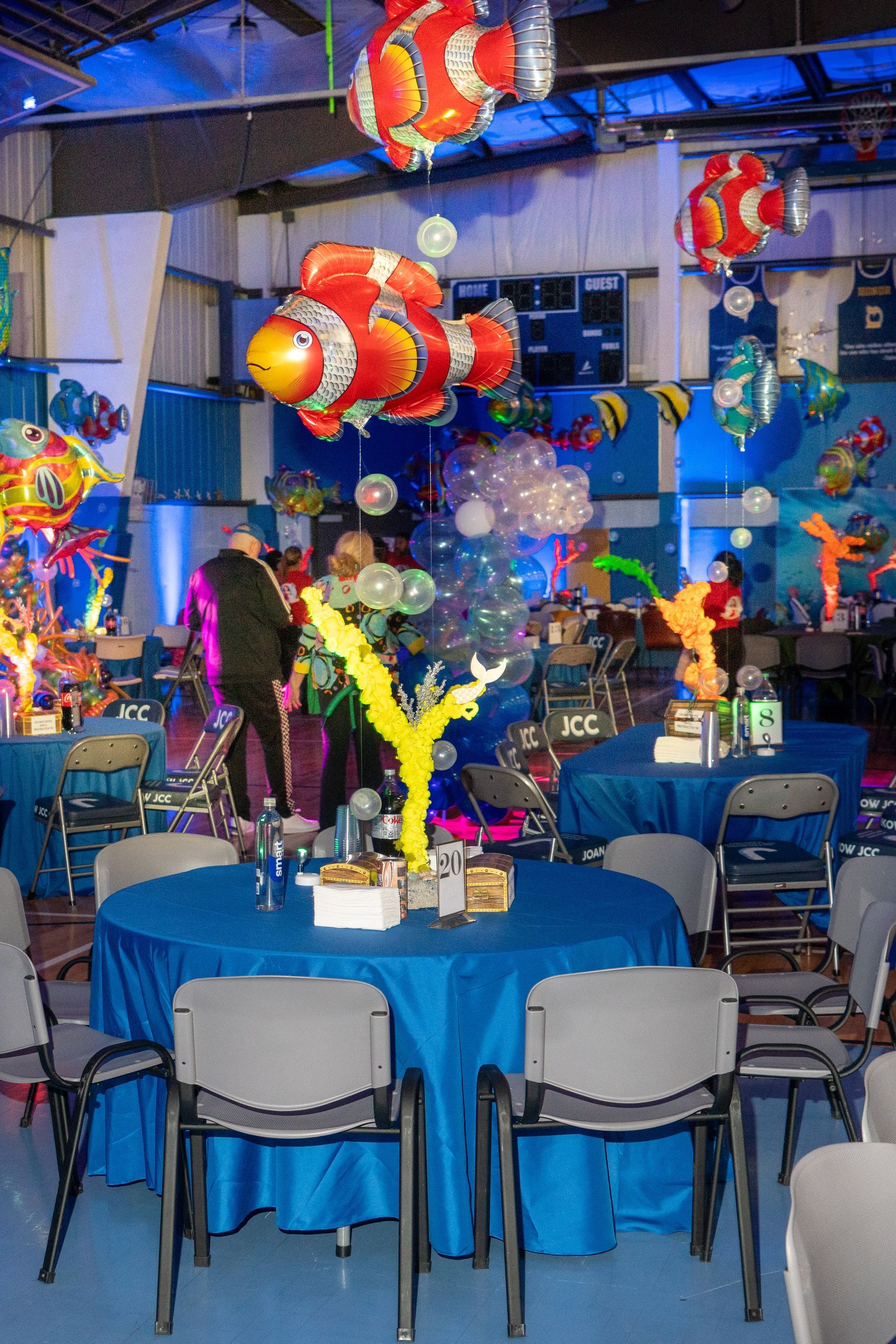 Event venue with blue tablecloths, clownfish balloons, and people.