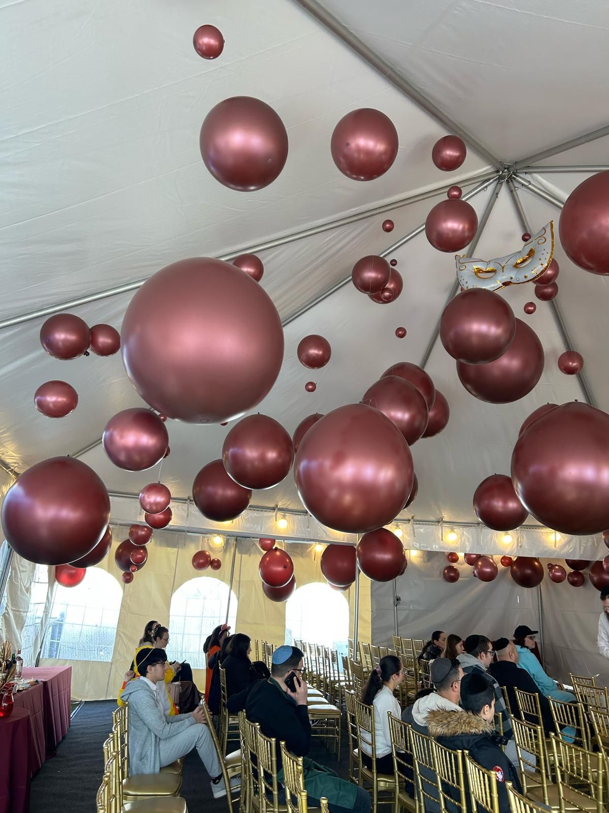 Maroon balloons floating inside a tent above a seated crowd at an event.