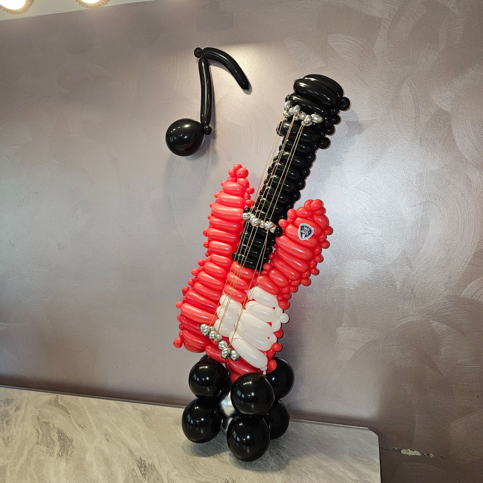 Balloon sculpture of a red and black guitar with a music note attached to a wall.