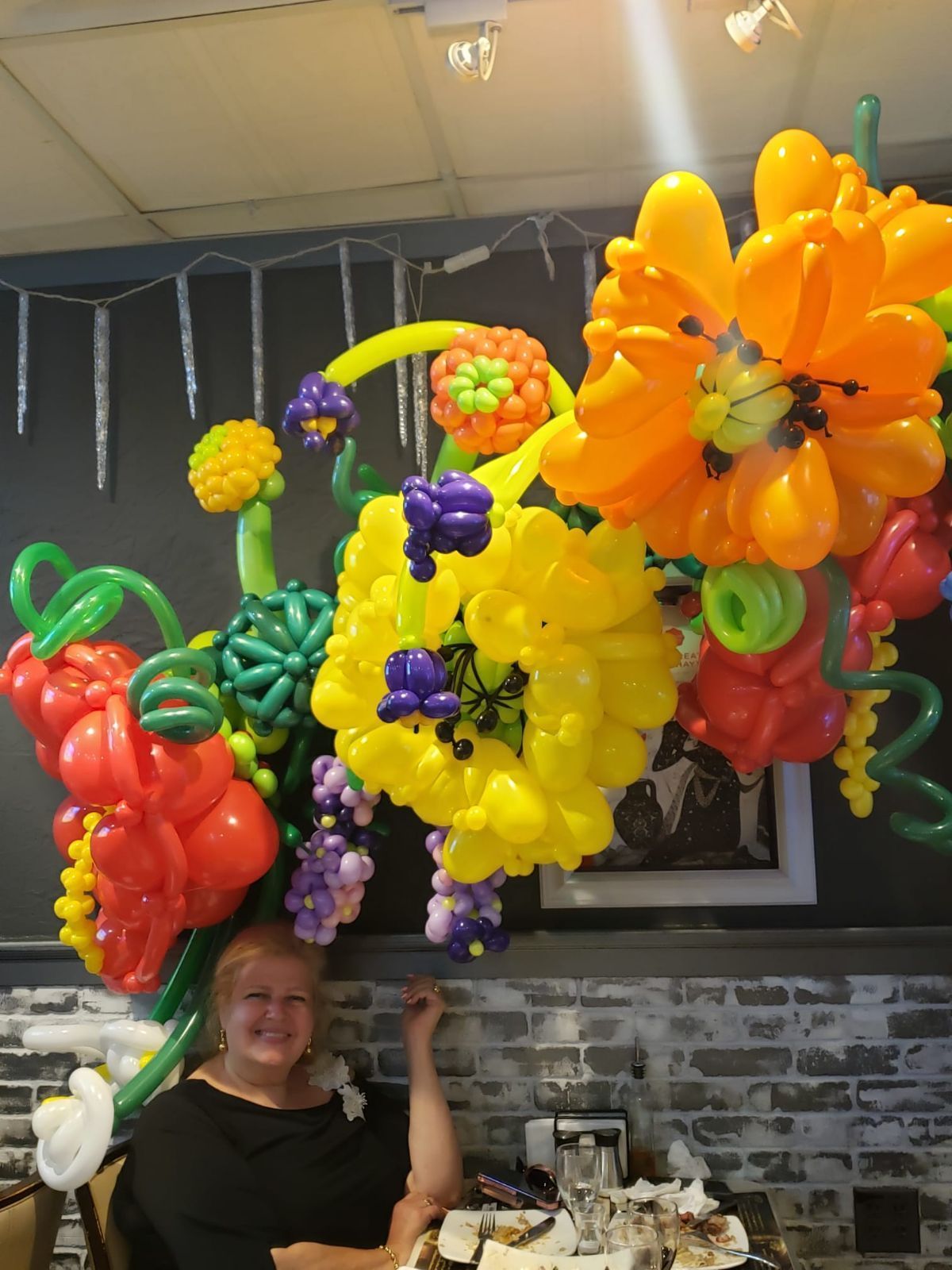 Woman smiling under a large balloon flower display, restaurant setting.