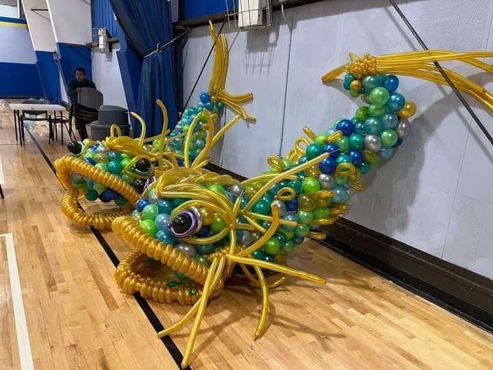 Two whimsical balloon fish sculptures in a gym. Yellow and blue balloons create the fish bodies.