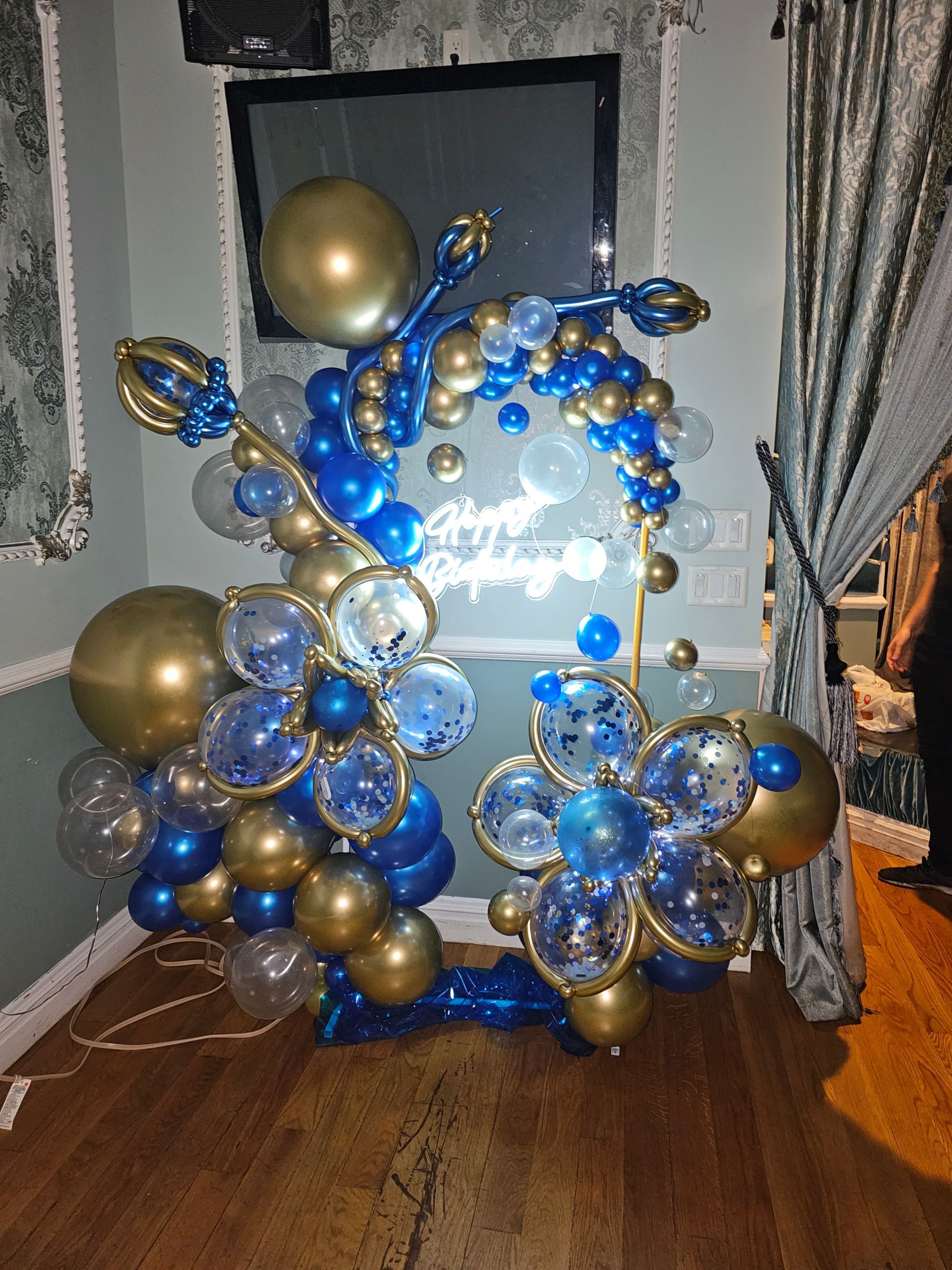 Blue and gold balloon arch and arrangements, with a sign, set up indoors for an event.