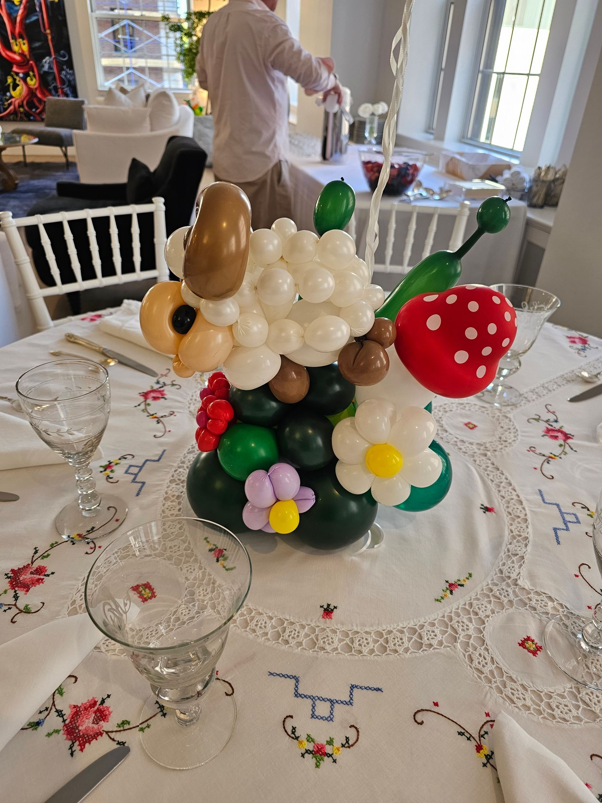 Balloon centerpiece in the shape of a sheep with flowers and a strawberry, on a table set for dining.