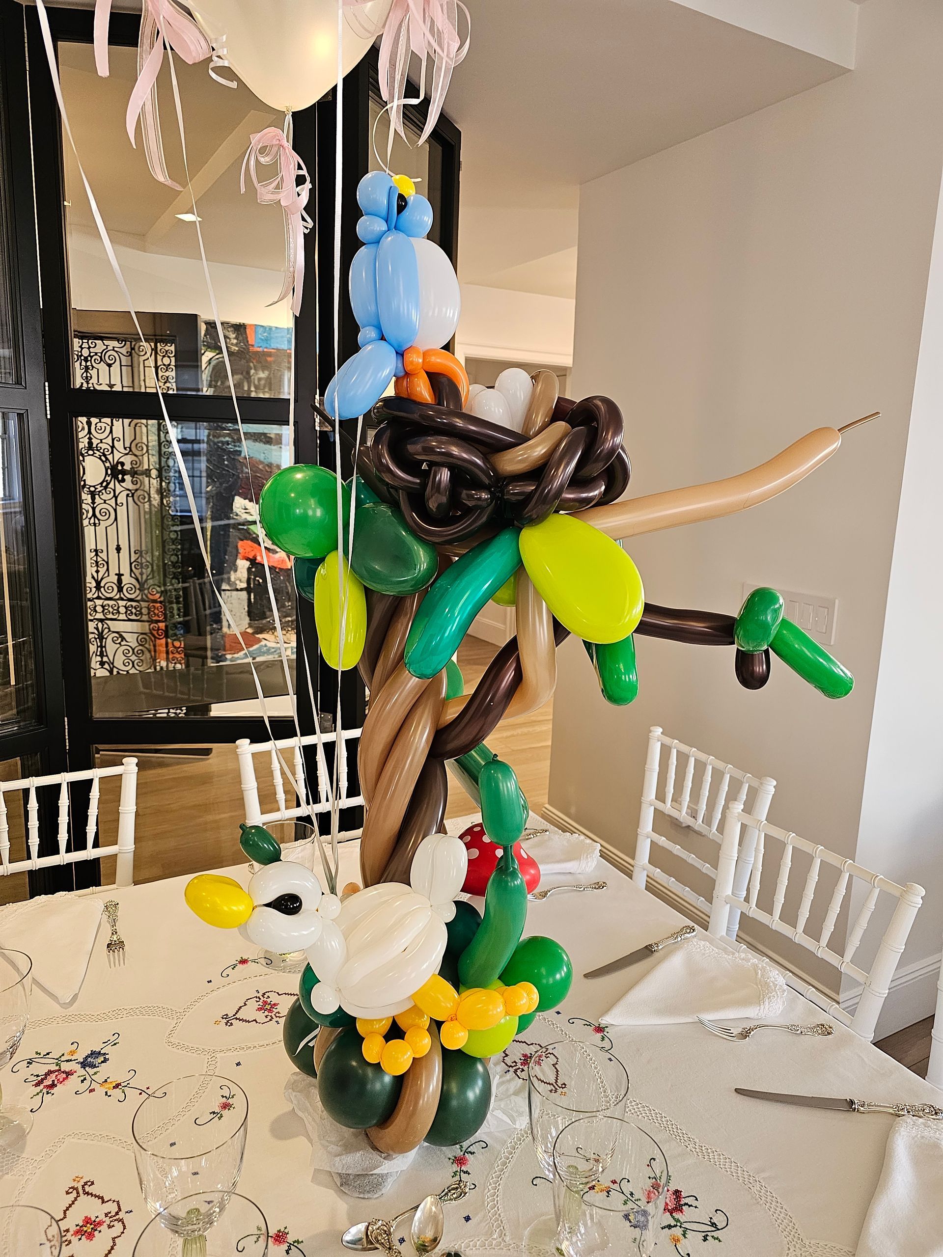Balloon sculpture of a bird, nest, and tree on a table, with other balloons hanging above.
