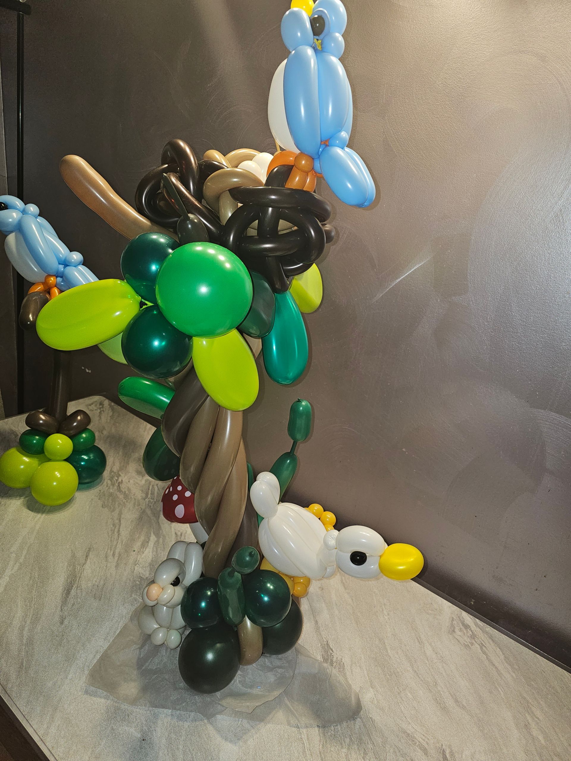 Balloon sculpture of a tree with birds, leaves, and a duck, in shades of green, brown, blue, and yellow.